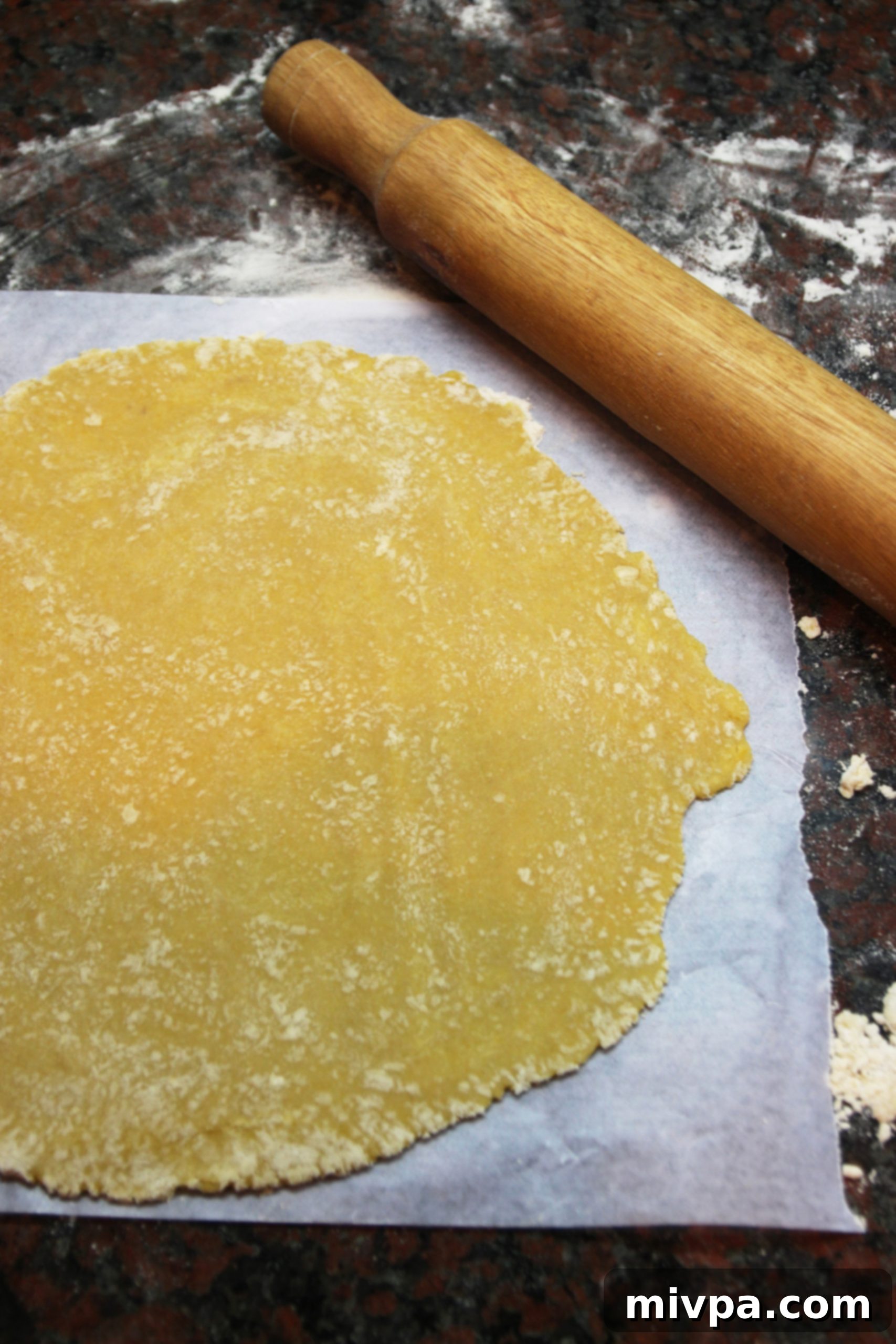 The chilled pastry dough being rolled out on a sheet of parchment paper to form the circular base for the galette.
