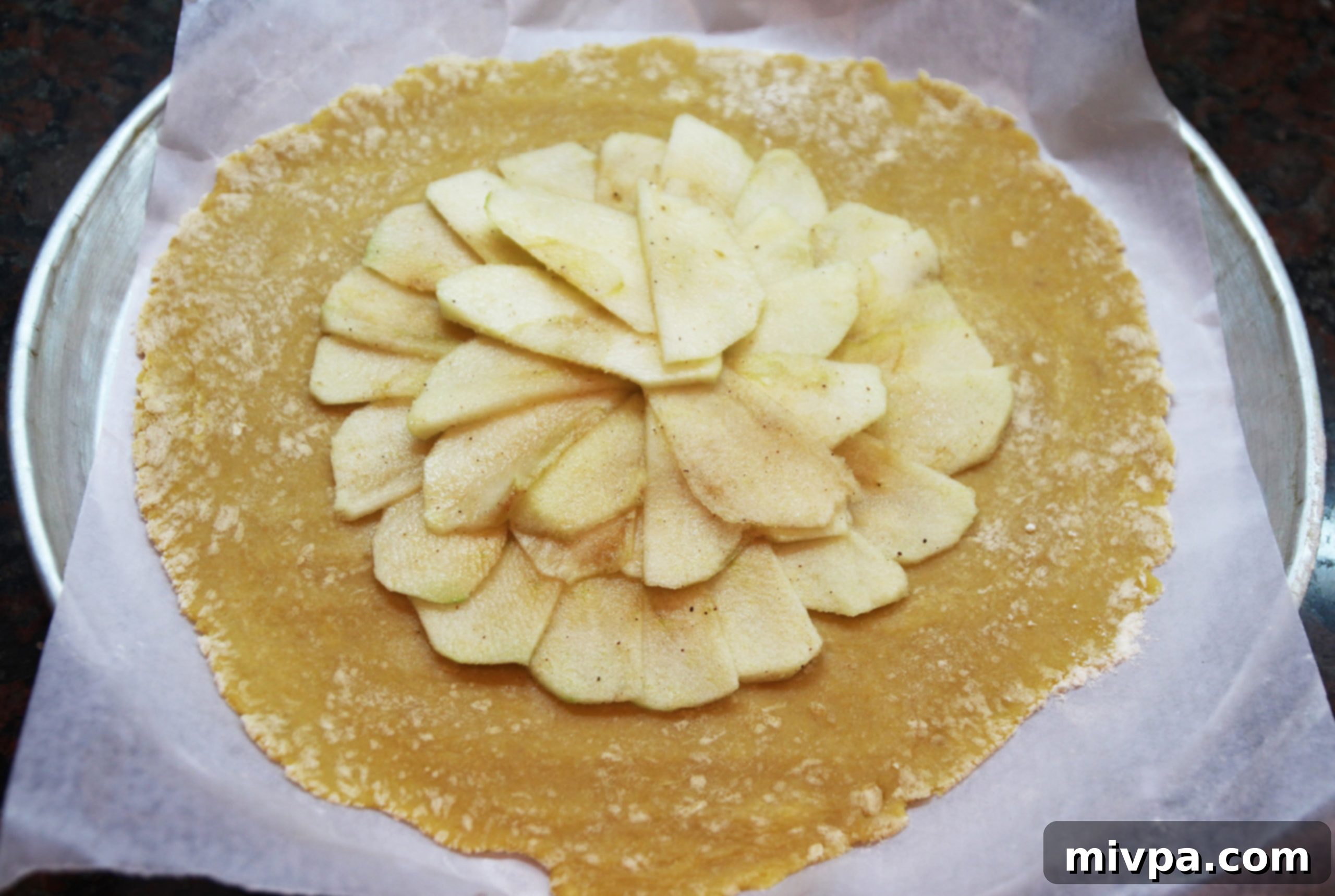 Carefully arranging thinly sliced apple pieces in an overlapping circular design on the rolled-out pastry dough, forming the galette filling.