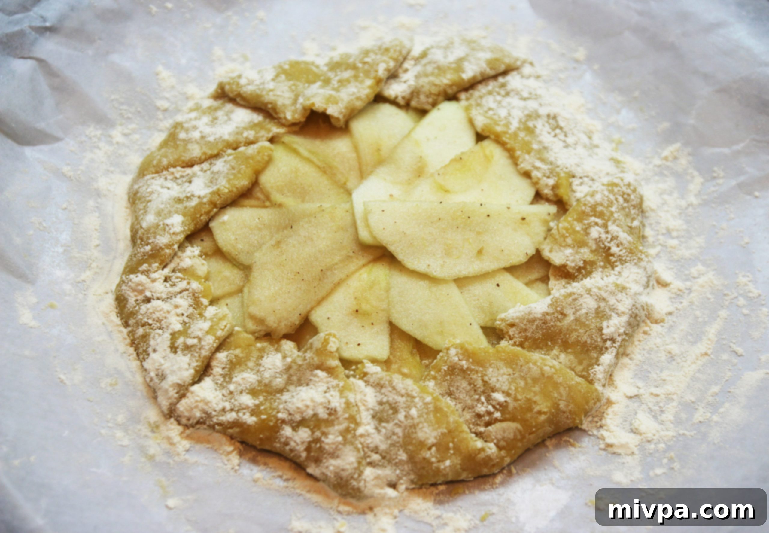 The edges of the pastry dough being folded inward over the apple filling to create the rustic crust of the galette, then sprinkled with sugar.