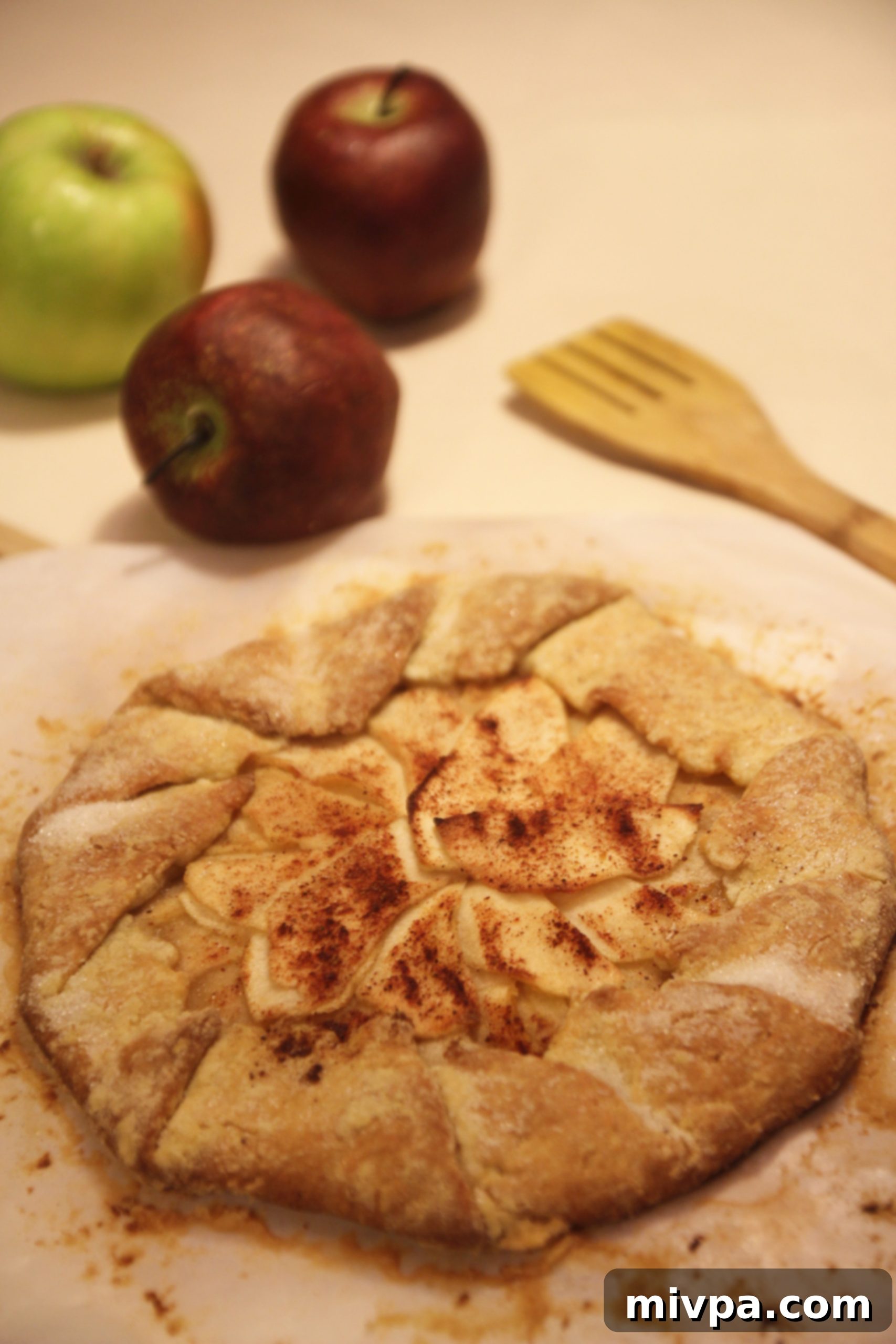 The finished, golden-brown Apple Cinnamon Galette, artfully arranged on a wooden board next to a cup of hot tea, ready for serving.
