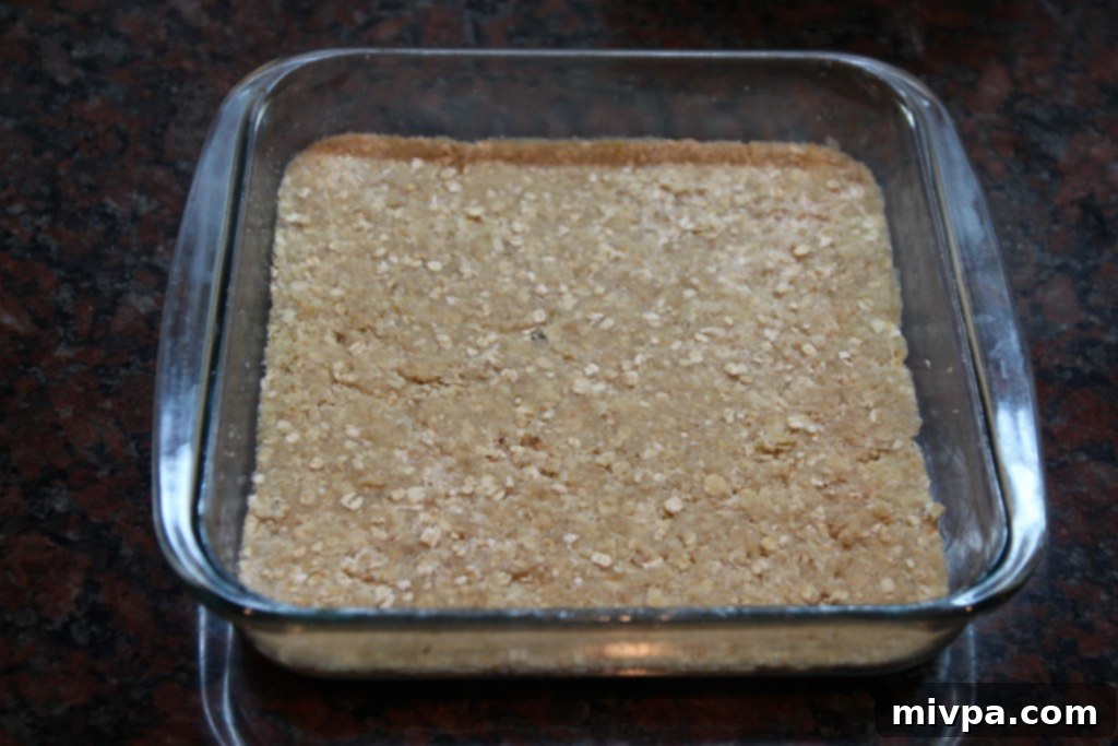 Pressing half of the oat crumb mixture into the baking dish for the bottom layer.