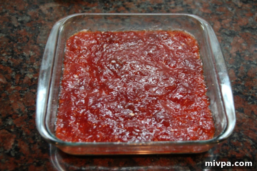 Spreading a thick layer of strawberry jam over the pressed oat crust.