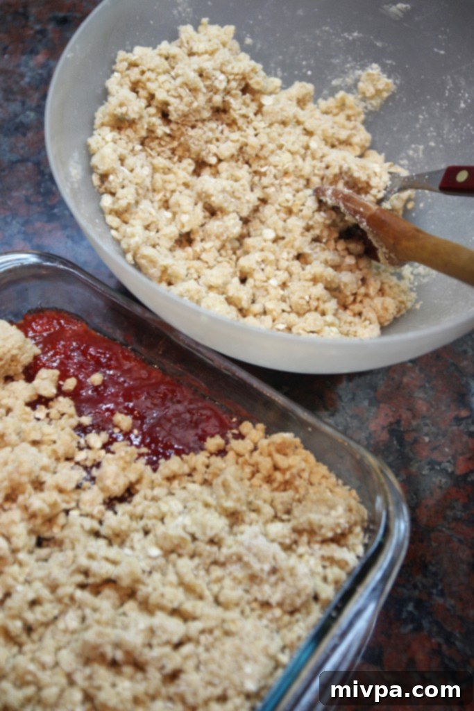 Spreading strawberry jam evenly over the oat crust base.