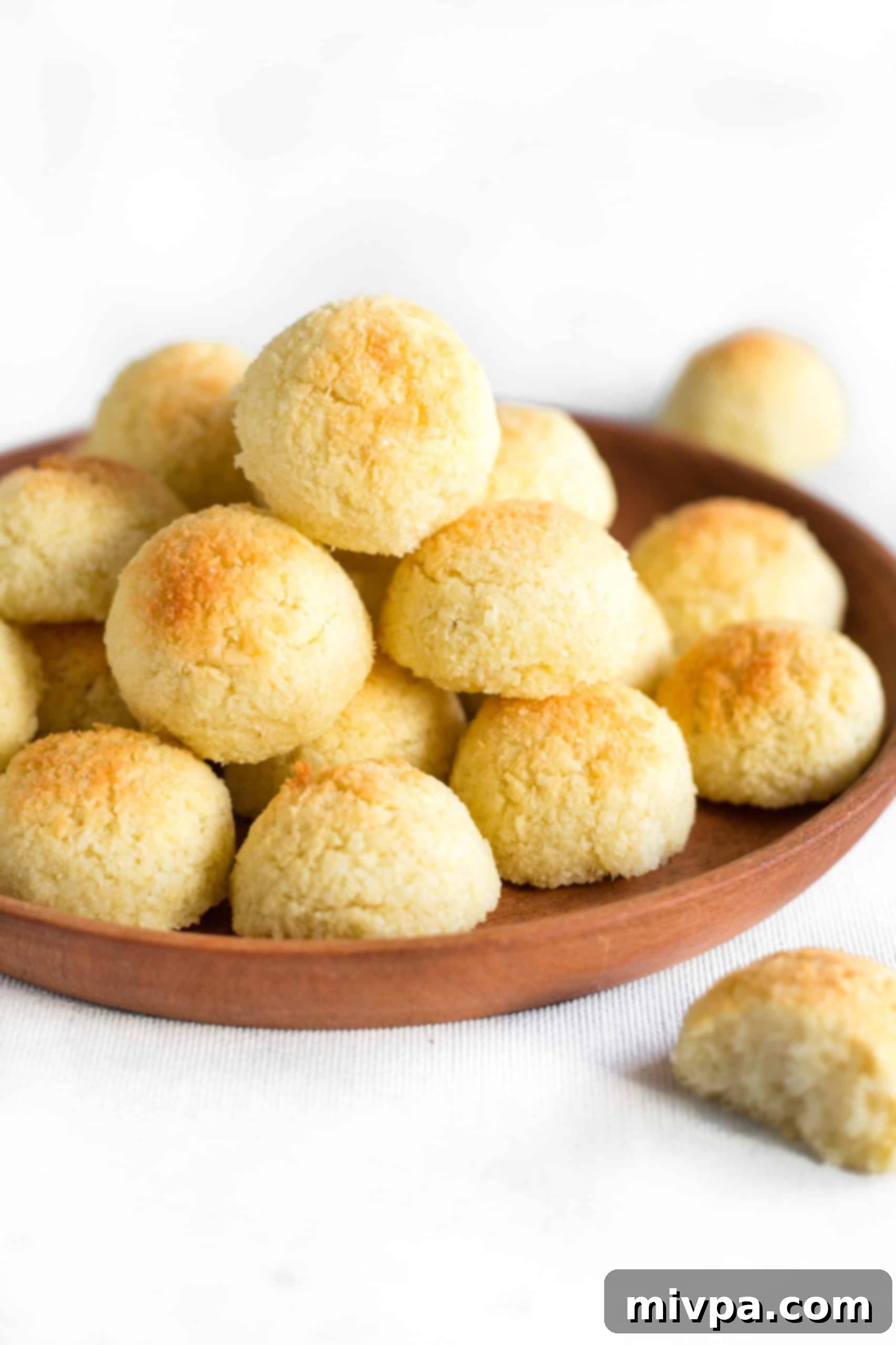 Easy Gluten-Free Coconut Macaroons (Dairy-Free) - Stacked on a Wooden Plate Gluten-free coconut macaroons piled high on a rustic wooden plate, showcasing their golden-brown exterior and inviting texture.