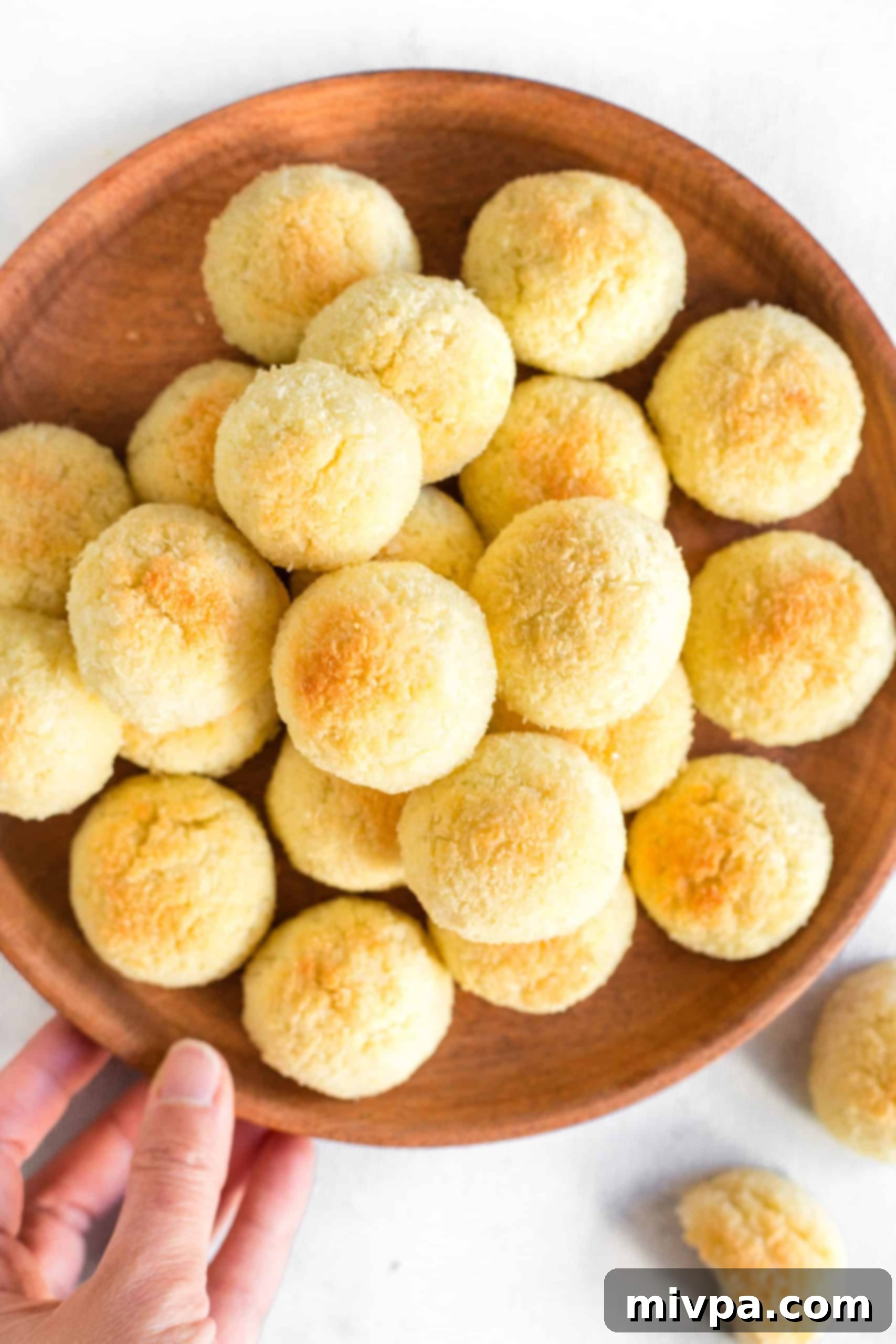 Easy Coconut Macaroons (Gluten-Free, Dairy-Free) - Platter A hand presenting a rustic wooden plate generously piled with easy, gluten-free coconut macaroons.