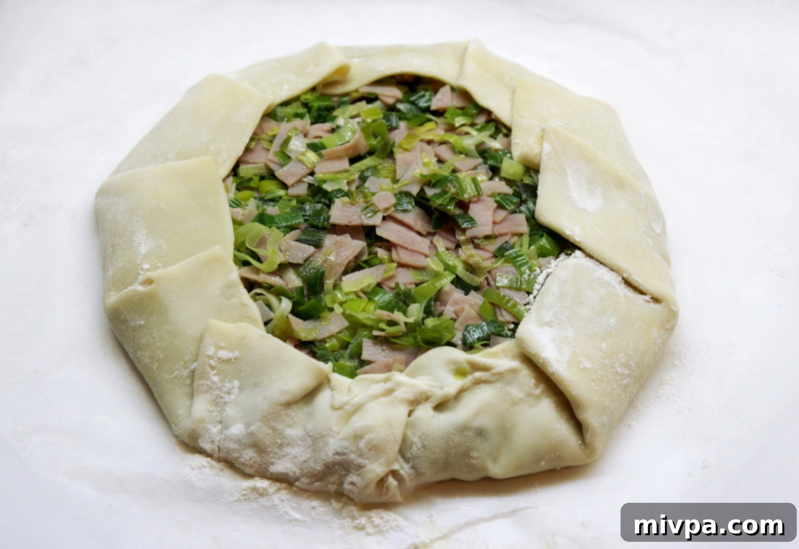 Edges of the pie crust folded over the leek and ham filling