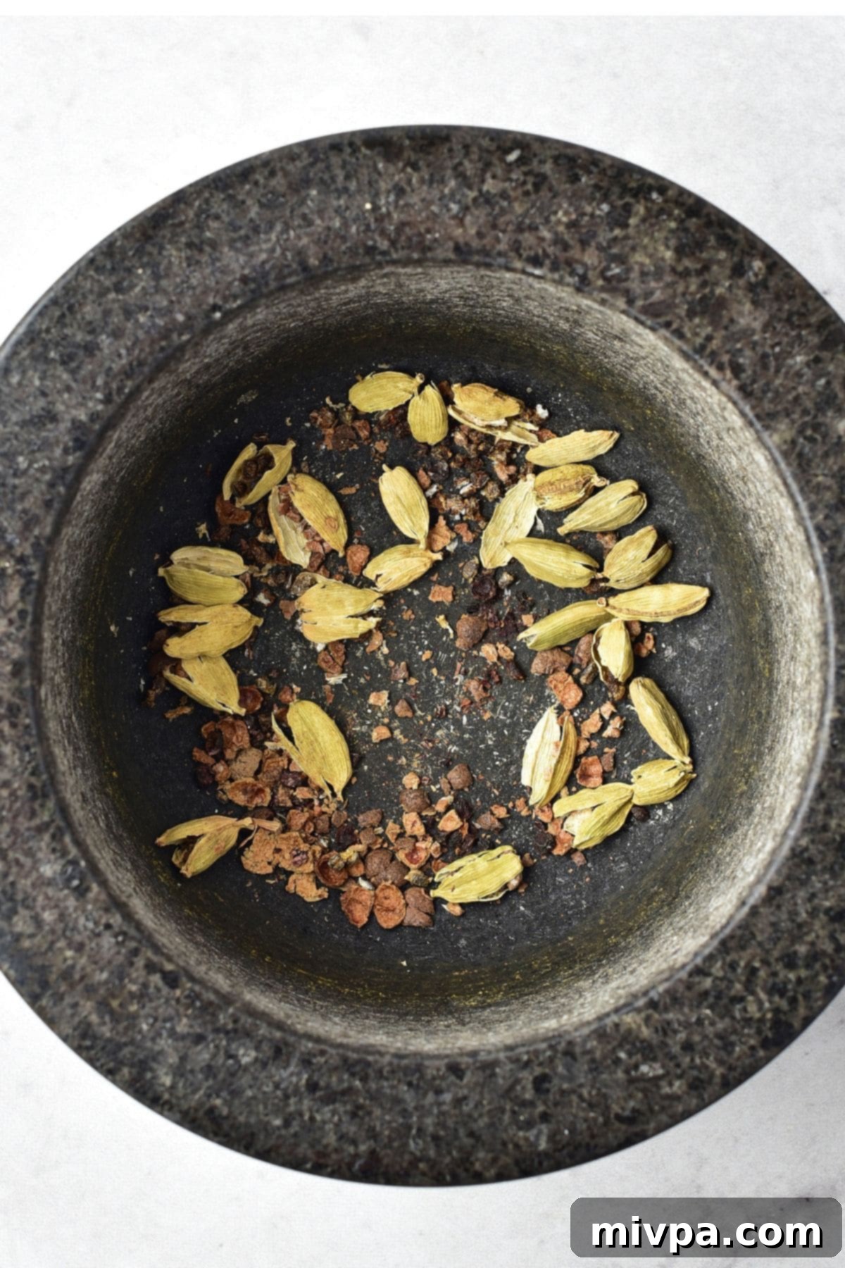 DIY Apple Pie Spice Blend Cardamom pods and whole allspice berries being crushed in a mortar with a pestle, releasing their natural fragrance.