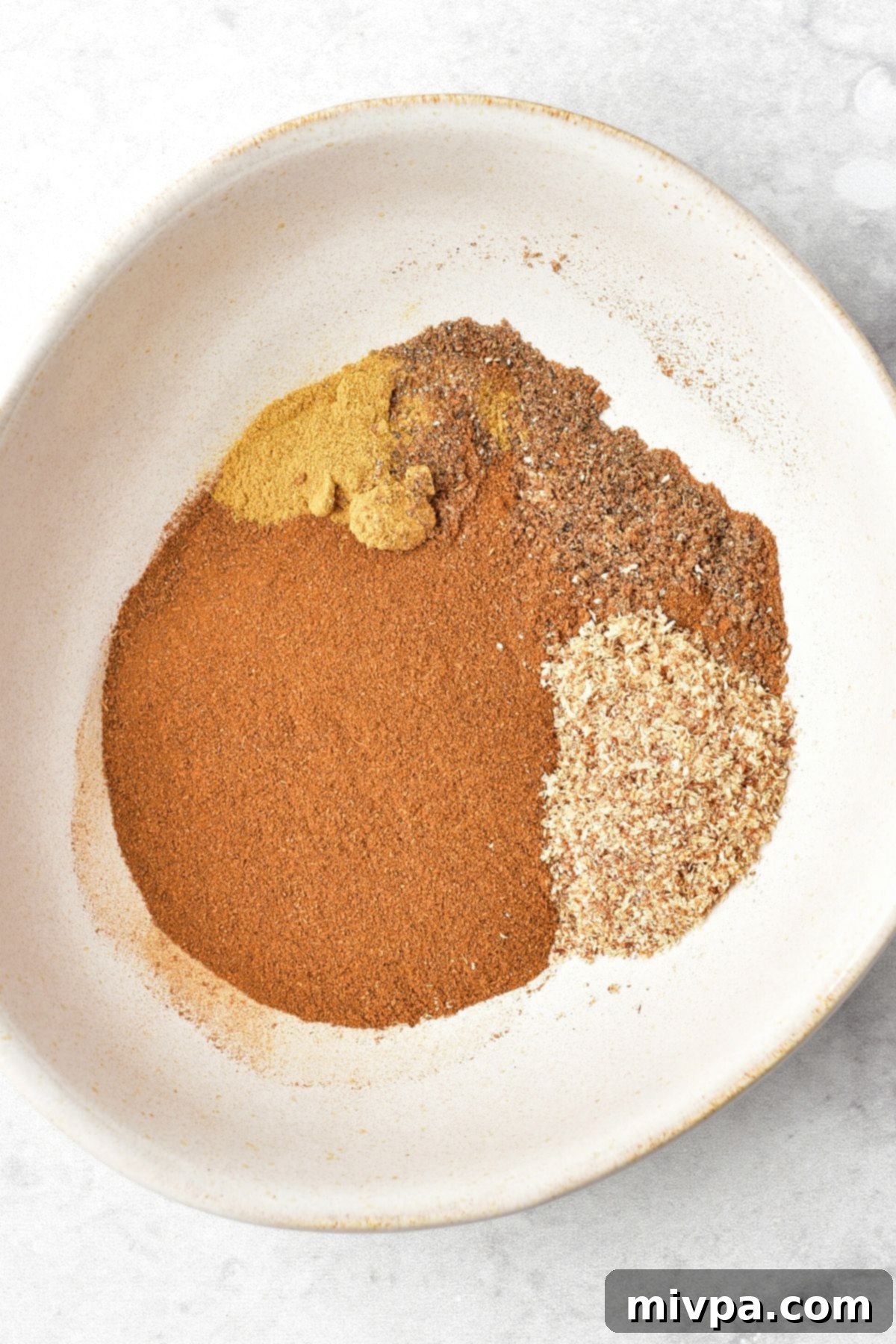 Homemade Apple Pie Spice Mix A mixing bowl with various ground spices, including cinnamon, ginger, and nutmeg, waiting to be combined.