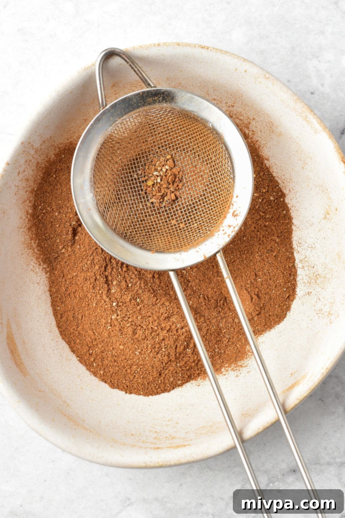 Easy Apple Pie Spice Blend Sifting a freshly made apple pie spice blend through a fine-mesh sieve to achieve a smooth, lump-free texture.