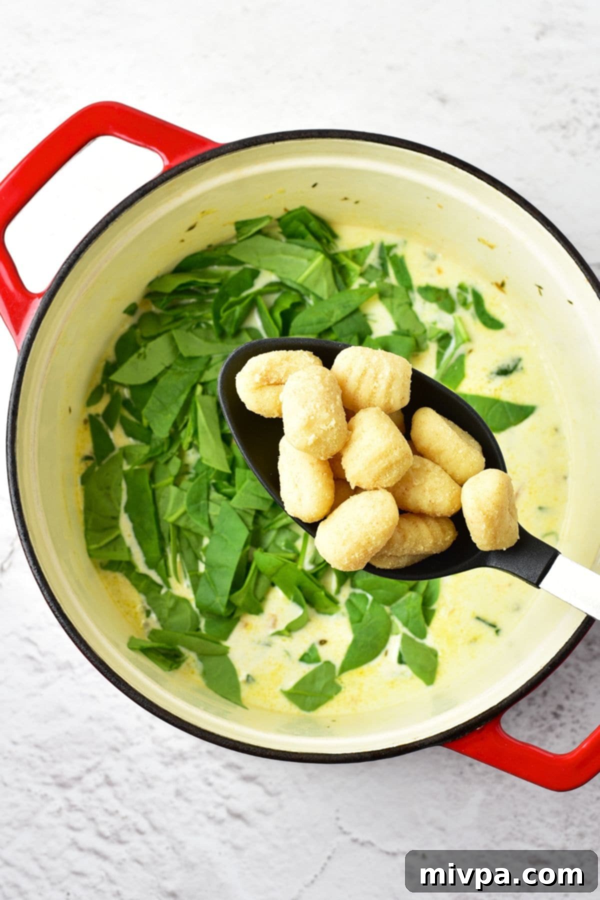 Gluten-Free Dairy-Free Creamy Chicken Gnocchi Soup 3 A ladle holding gluten-free potato gnocchi above the pot of soup, about to be stirred in for cooking.