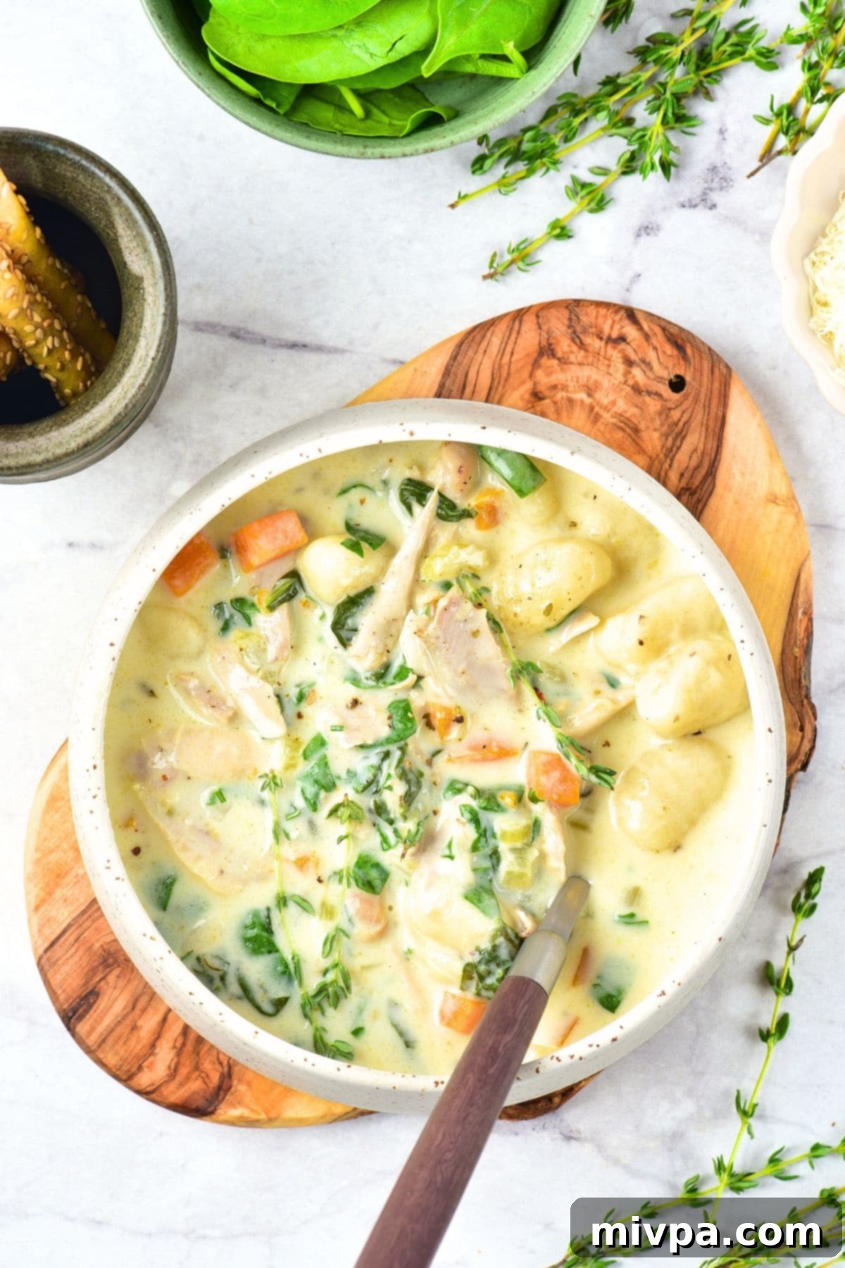 Hearty Chicken and Gnocchi Soup (Gluten-Free, Dairy-Free) A rustic bowl of chicken and gnocchi soup on a wooden board, with steam rising, indicating warmth.