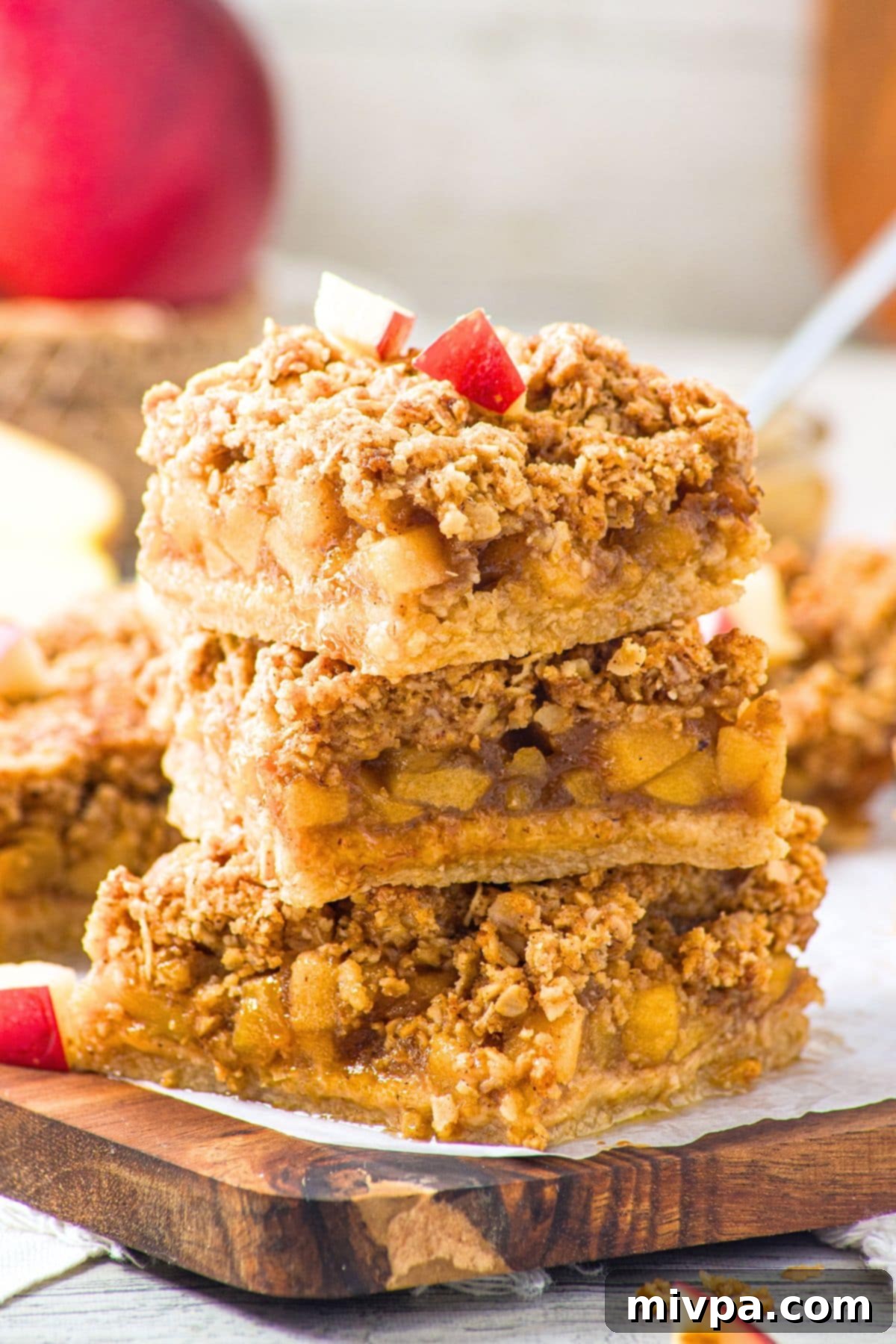 Apple Oatmeal Bars (Gluten-Free, Vegan) A stack of apple oatmeal bars on parchment-lined wooden board, showcasing their golden-brown crust and juicy apple filling.