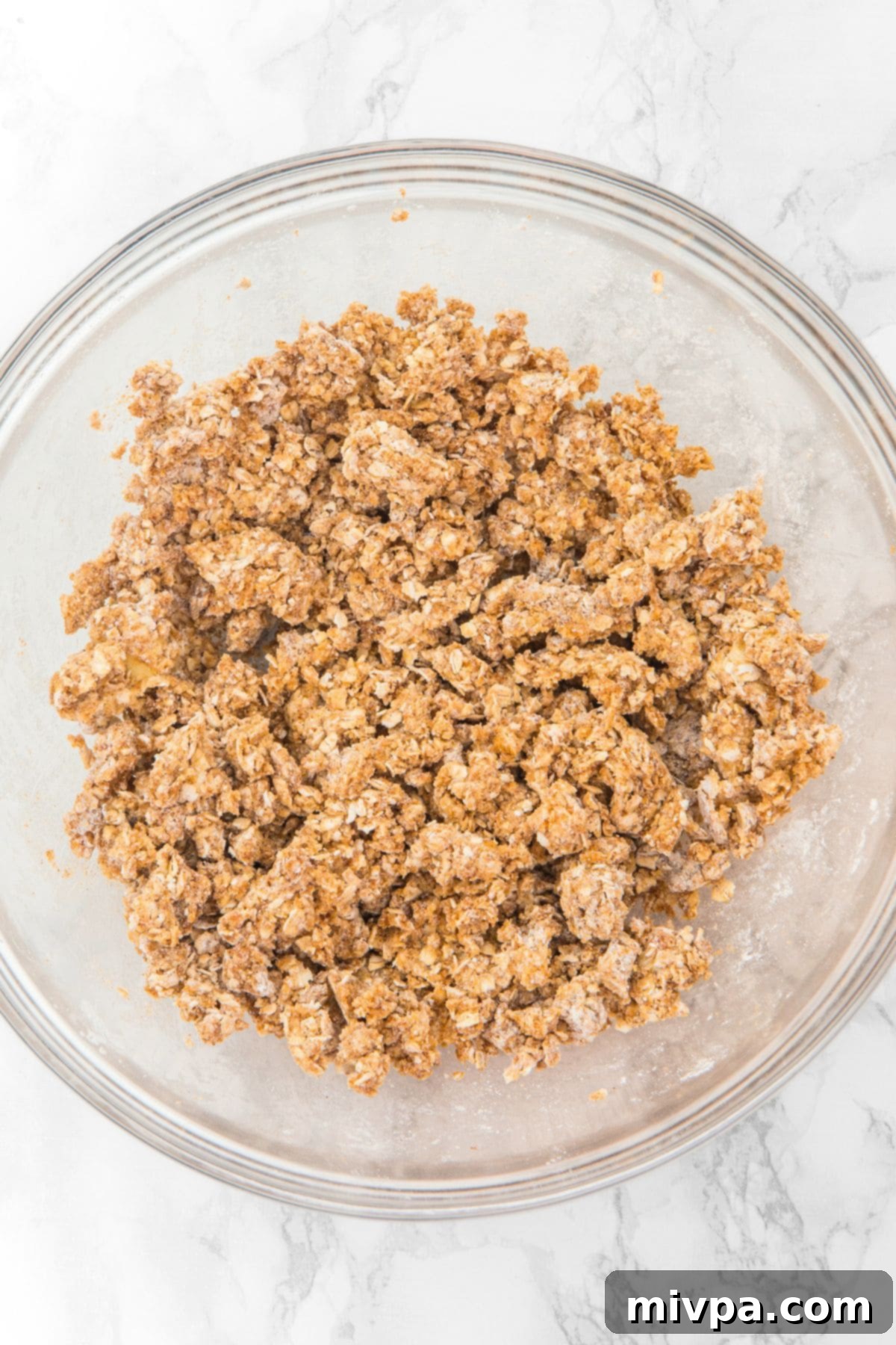 Easy Apple Oat Bars A glass bowl filled with the crumble topping mixture, consisting of instant oats, cornstarch, brown sugar, cinnamon, salt, and butter, lightly mixed.