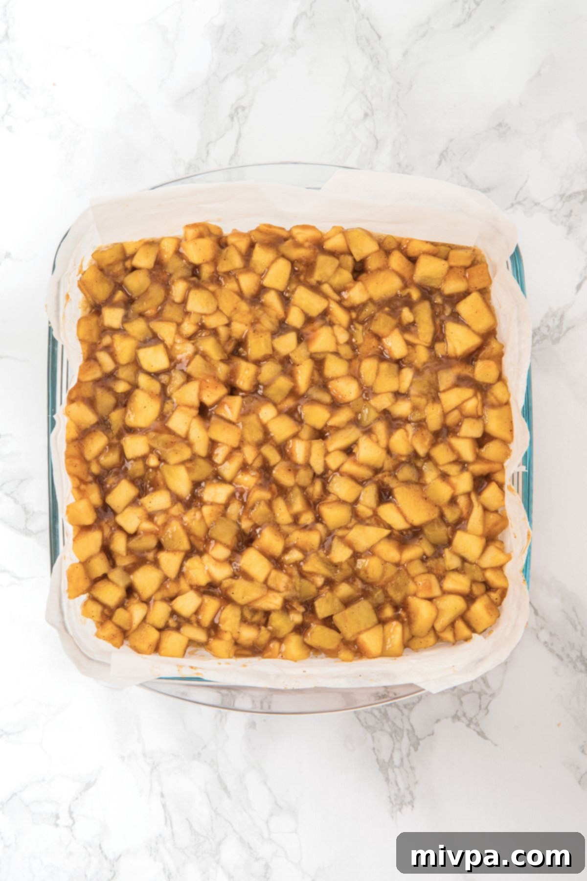 Wholesome Gluten-Free Vegan Apple Oat Bars 4 The cooked apple filling spread evenly over the pre-baked crust in the parchment-lined glass pan, forming the middle layer of the bars.