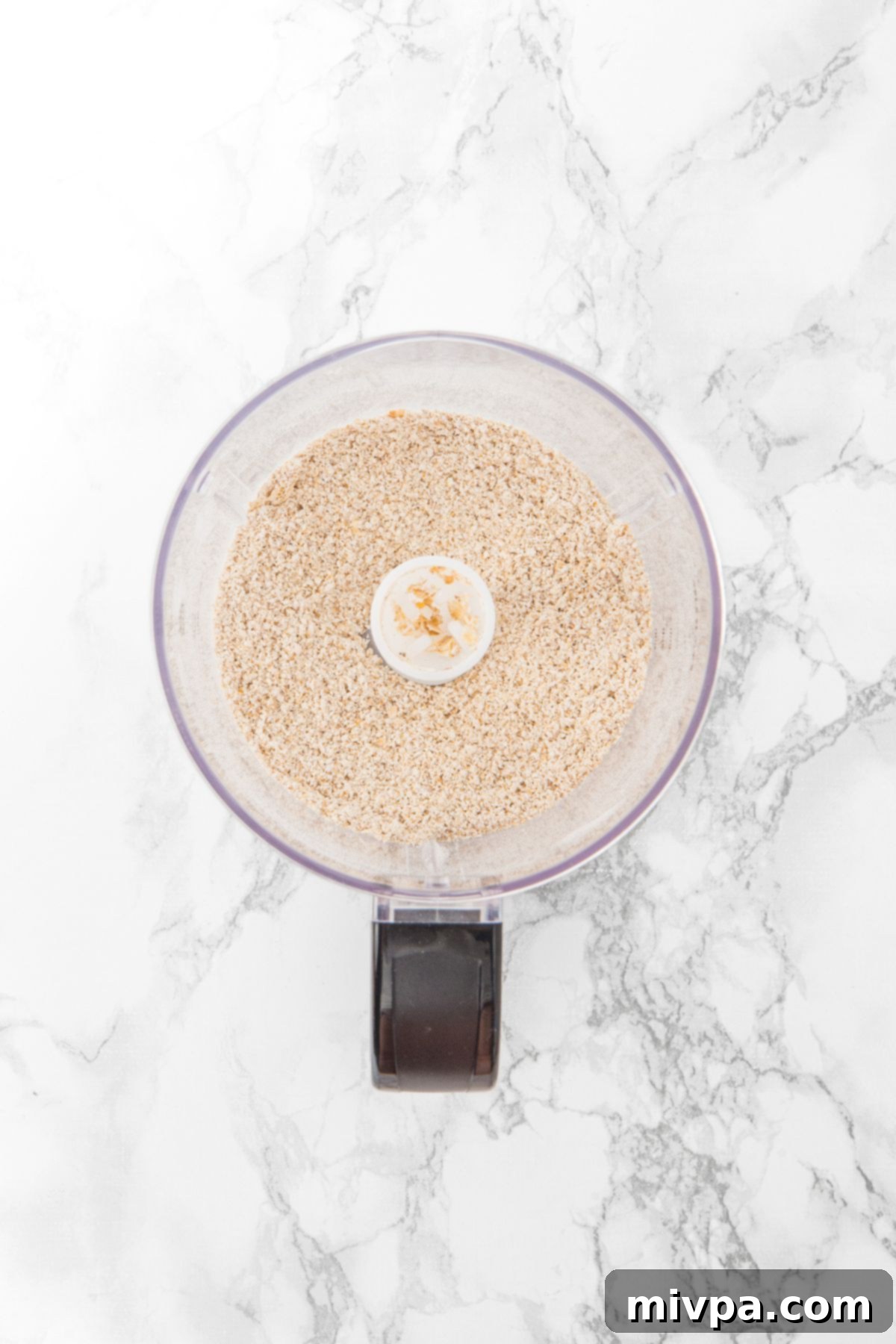 How to Make Apple Oatmeal Bars (Gluten-Free, Vegan) Finely processed gluten-free quick oats, resembling flour, in a food processor, ready for the crust mixture.