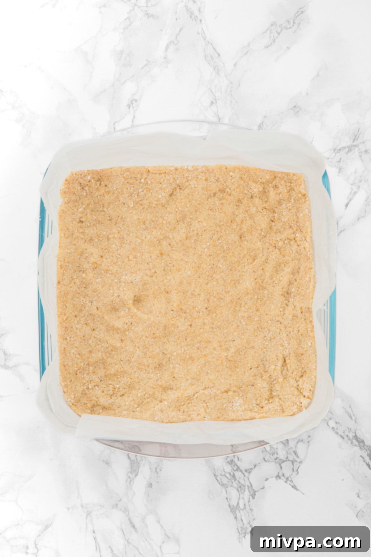 Apple Oatmeal Bars Recipe The crust mixture pressed evenly into the bottom of a parchment-lined glass baking pan, ready for its initial bake.