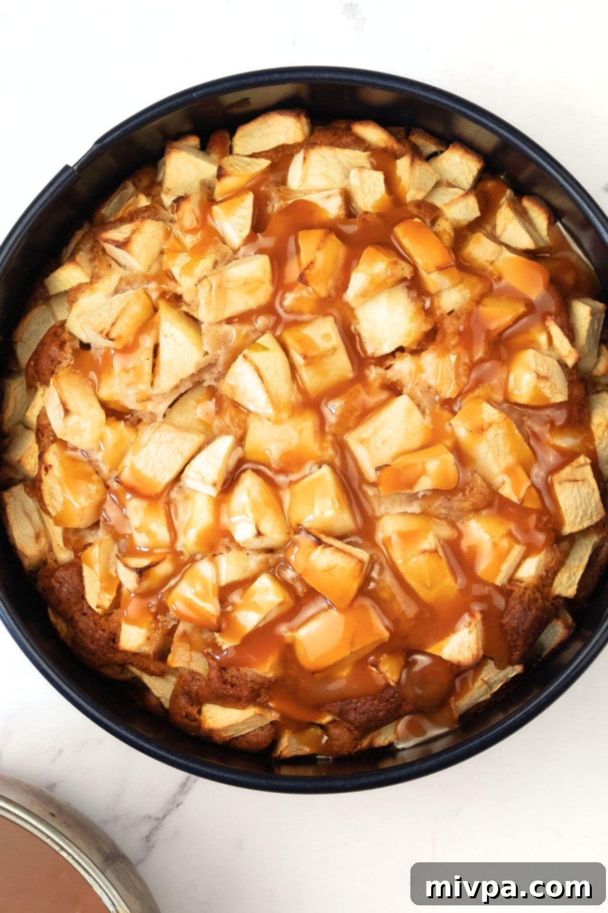 Caramel Drizzled Over Apple Cake Warm, glistening caramel sauce being poured generously over the baked apple cake, coating the apple pieces.