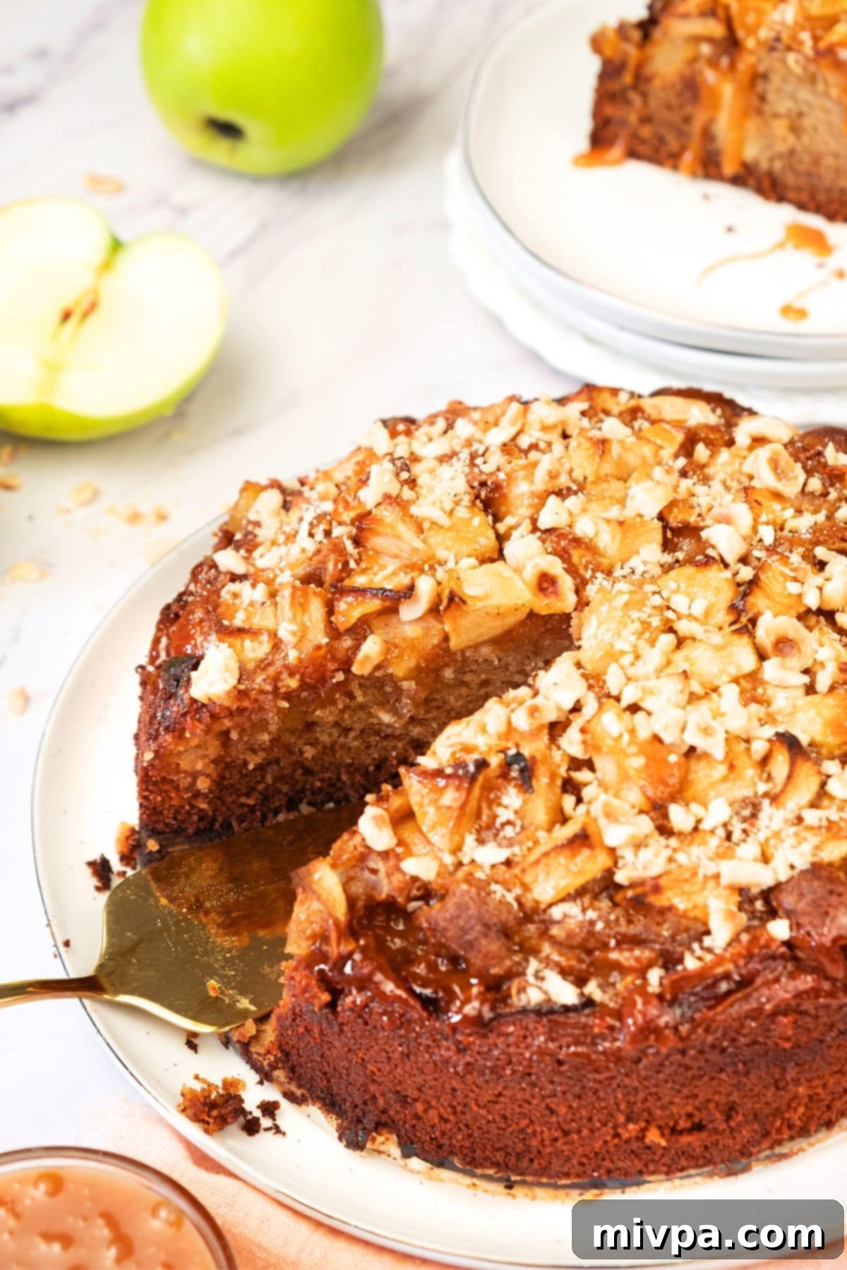 Cooling and Serving Swedish Äppelkaka A half-sliced Swedish apple cake on a cake stand, garnished with powdered sugar and nuts, ready to be served.