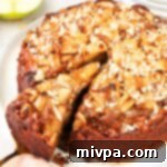 A hand reaching for a slice of the rustic Swedish apple cake, showcasing its inviting texture and golden caramel drizzle.