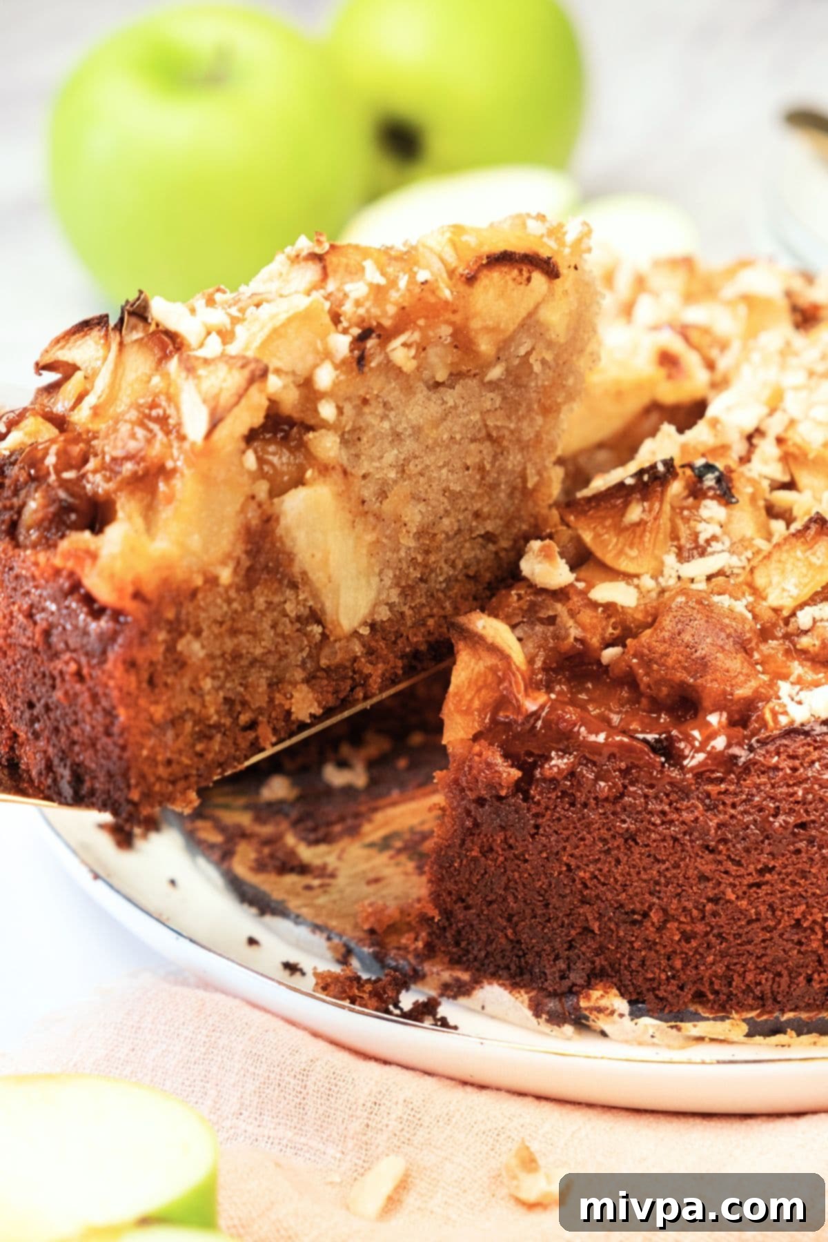 Gluten-Free Swedish Apple Cake Slice A hand holding up a perfect slice of gluten-free Swedish apple cake from a cake stand, ready to be enjoyed.