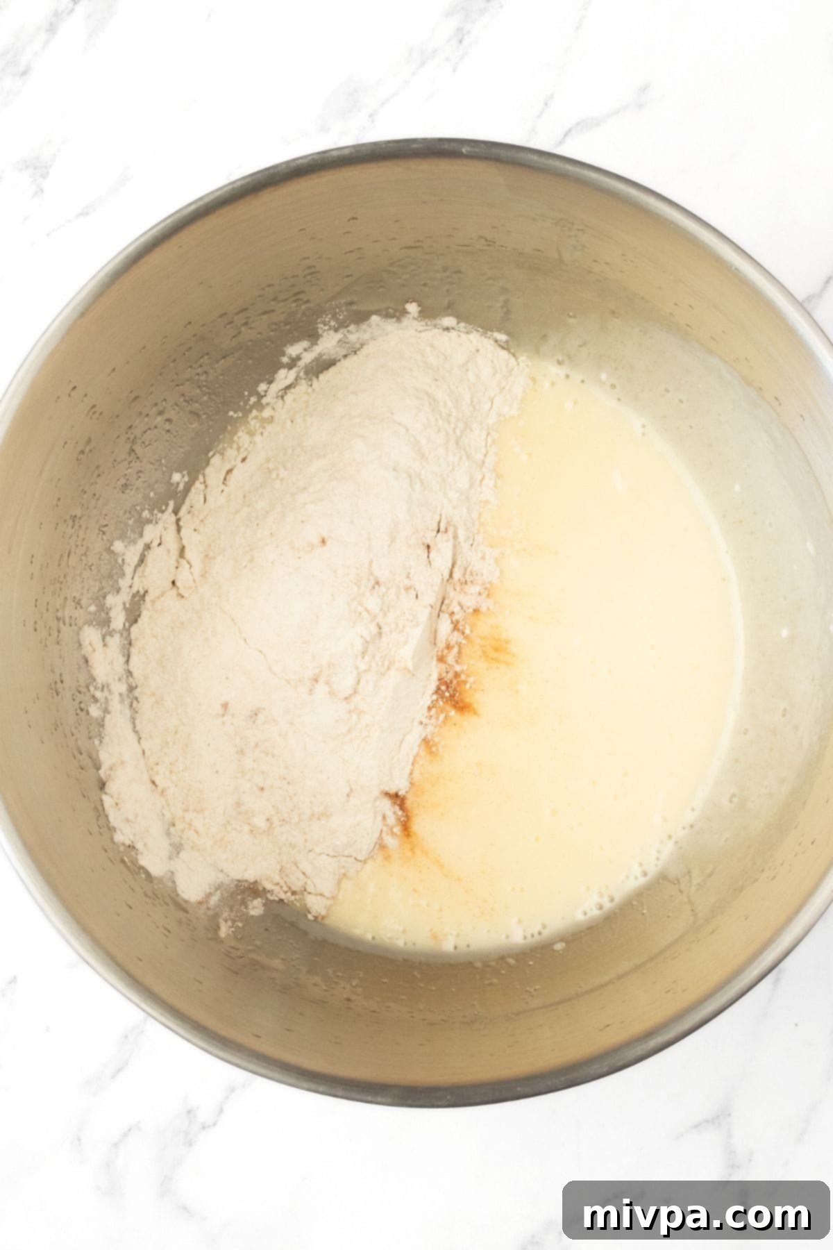 Adding Dry Ingredients to Apple Swedish Cake Batter Gluten-free flour mixture piled on top of the wet cake batter in a bowl.