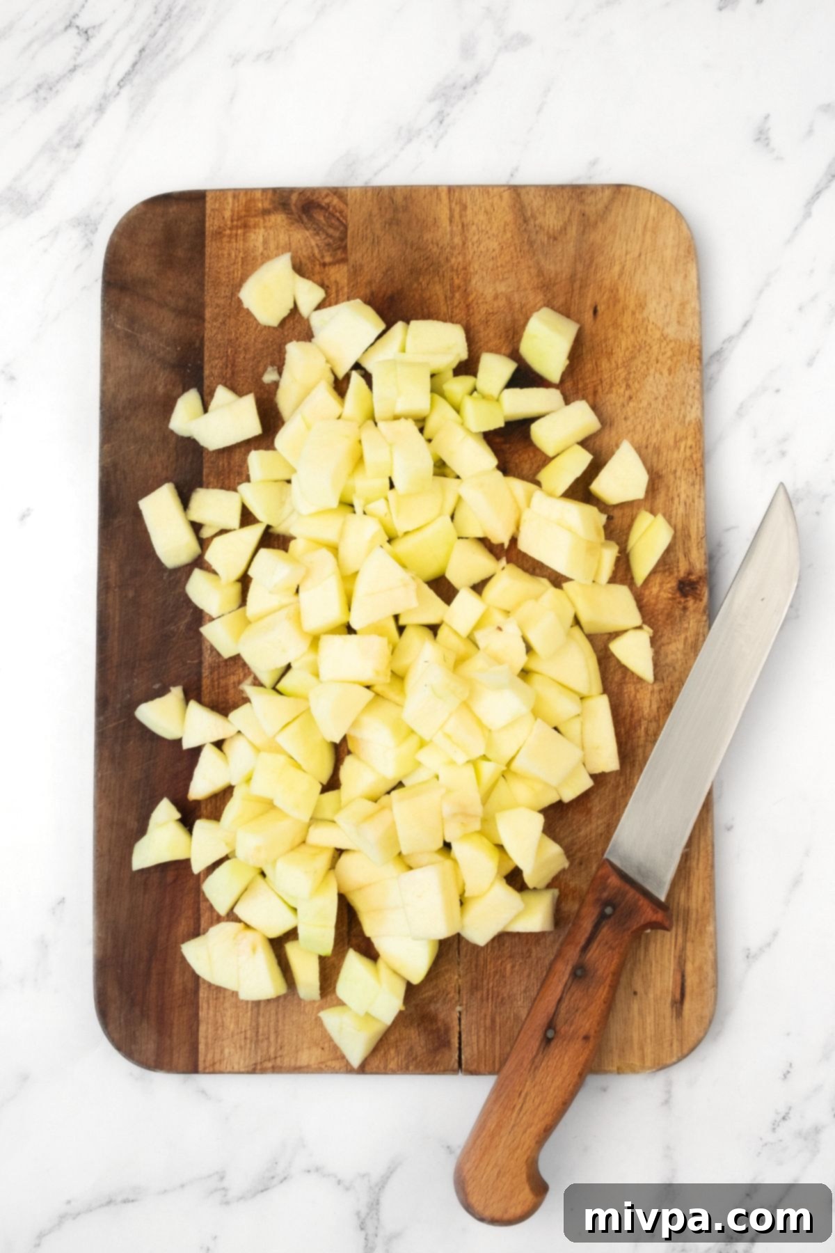 Prepping Apples for Swedish Apple Cake Freshly peeled, cored, and finely chopped apples on a wooden cutting board, ready for the cake.