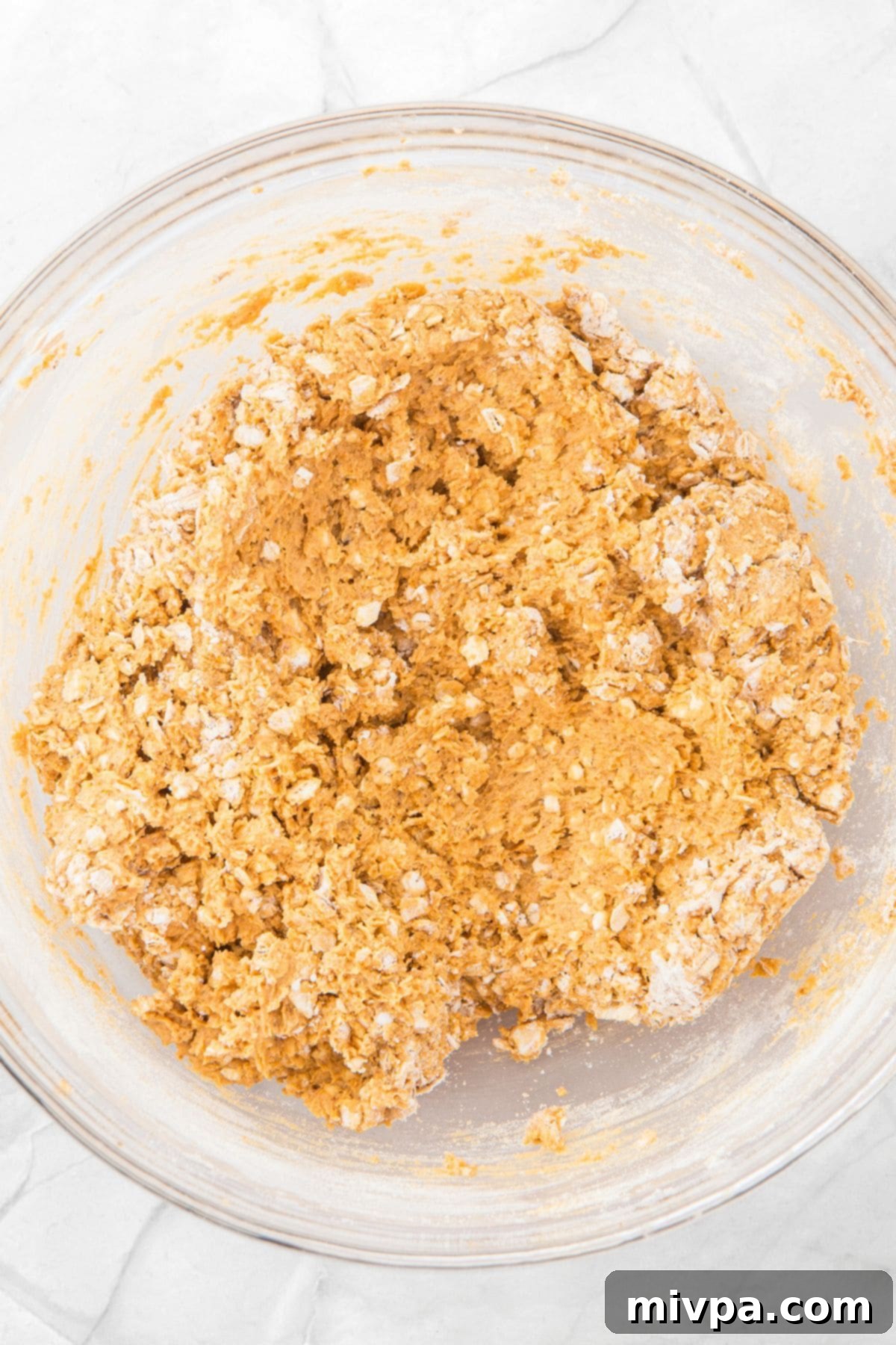 A glass bowl filled with cookie dough, showing the texture after dry ingredients have been added.