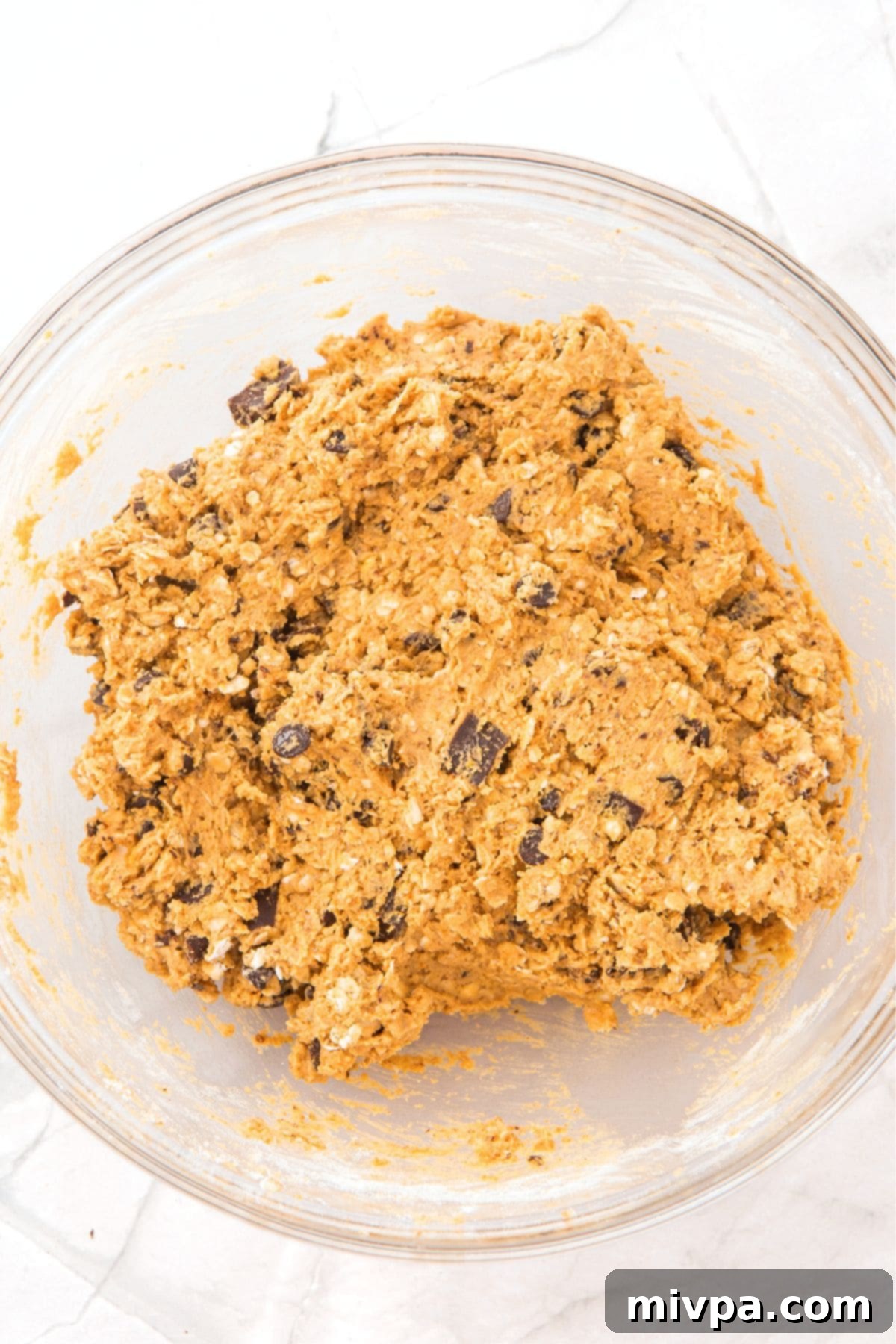 Chocolate chip cookie dough mixture in a glass bowl, with visible chunks of chocolate.