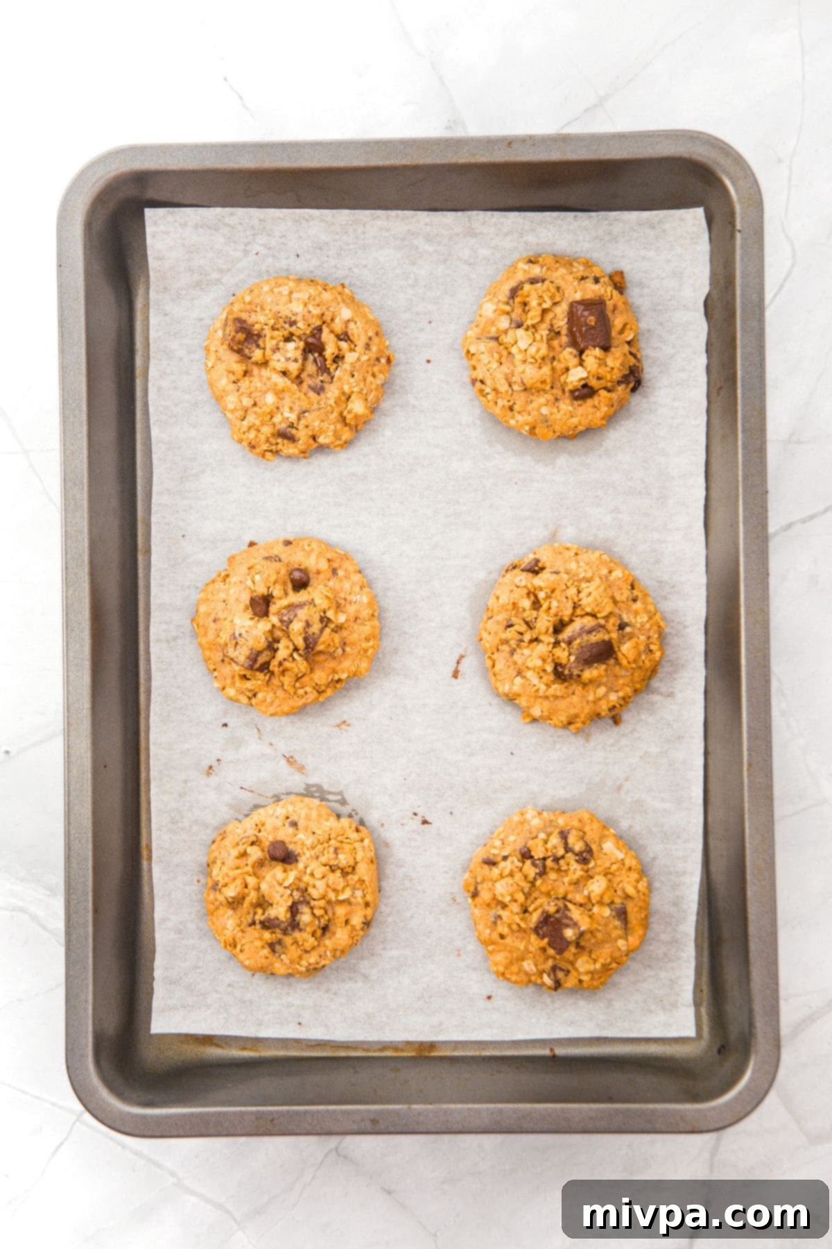 Freshly baked cookies on a parchment-lined baking sheet, golden brown with melted chocolate.