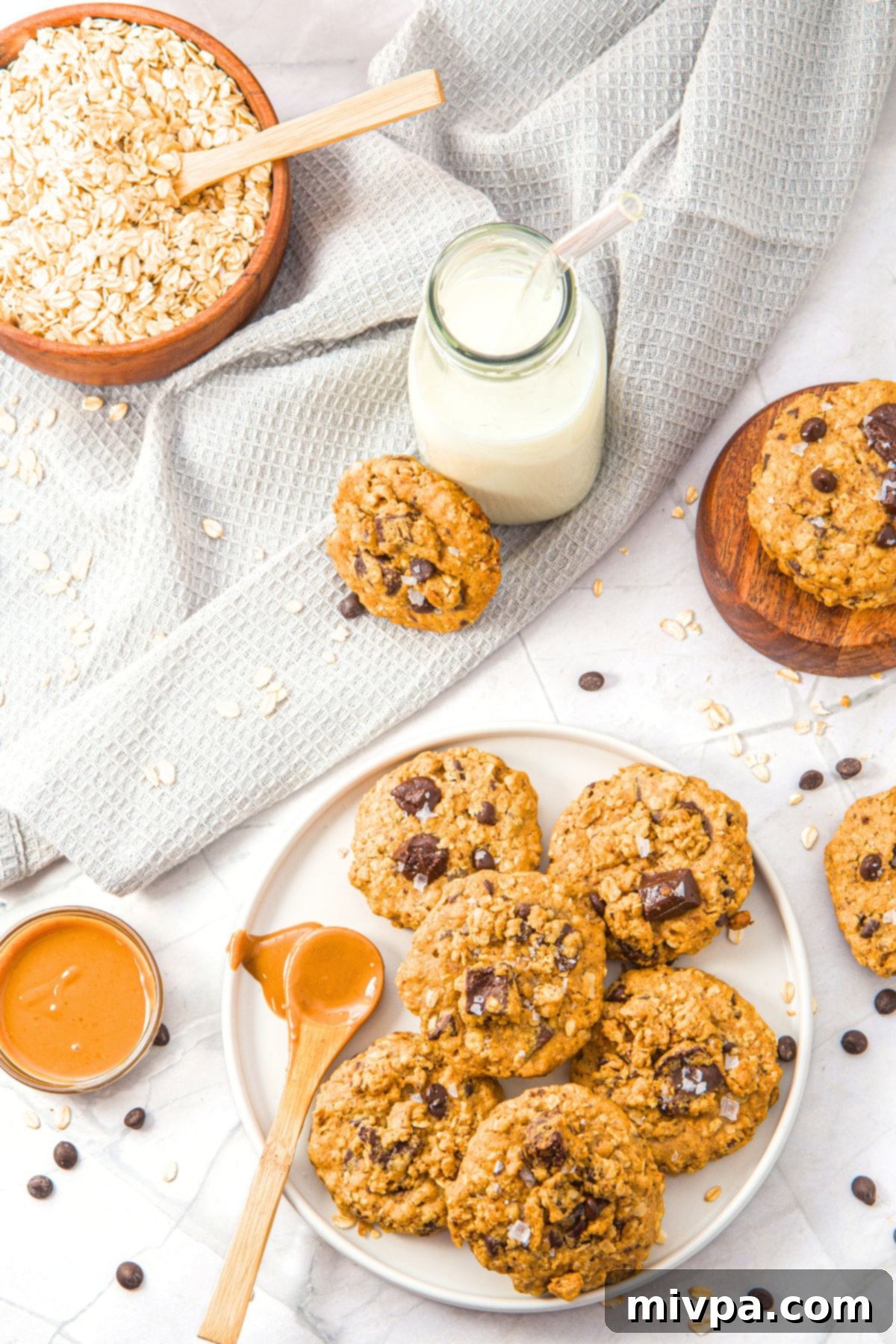 A plate of oatmeal peanut butter cookies with a spoon of peanut butter and chocolate chunks scattered around