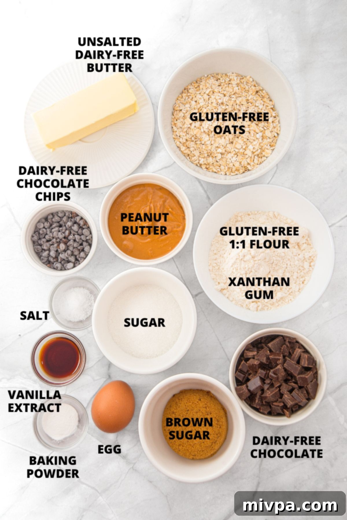 Ingredients for peanut butter oatmeal cookies recipe laid out neatly on a marble board, including flour, oats, peanut butter, butter, sugars, and chocolate.