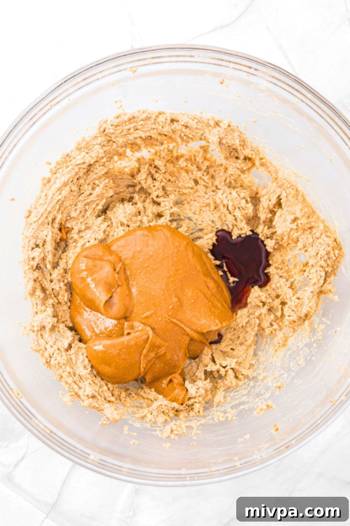 Creamy peanut butter and a drizzle of vanilla extract being added on top of the whipped butter and sugar mixture.