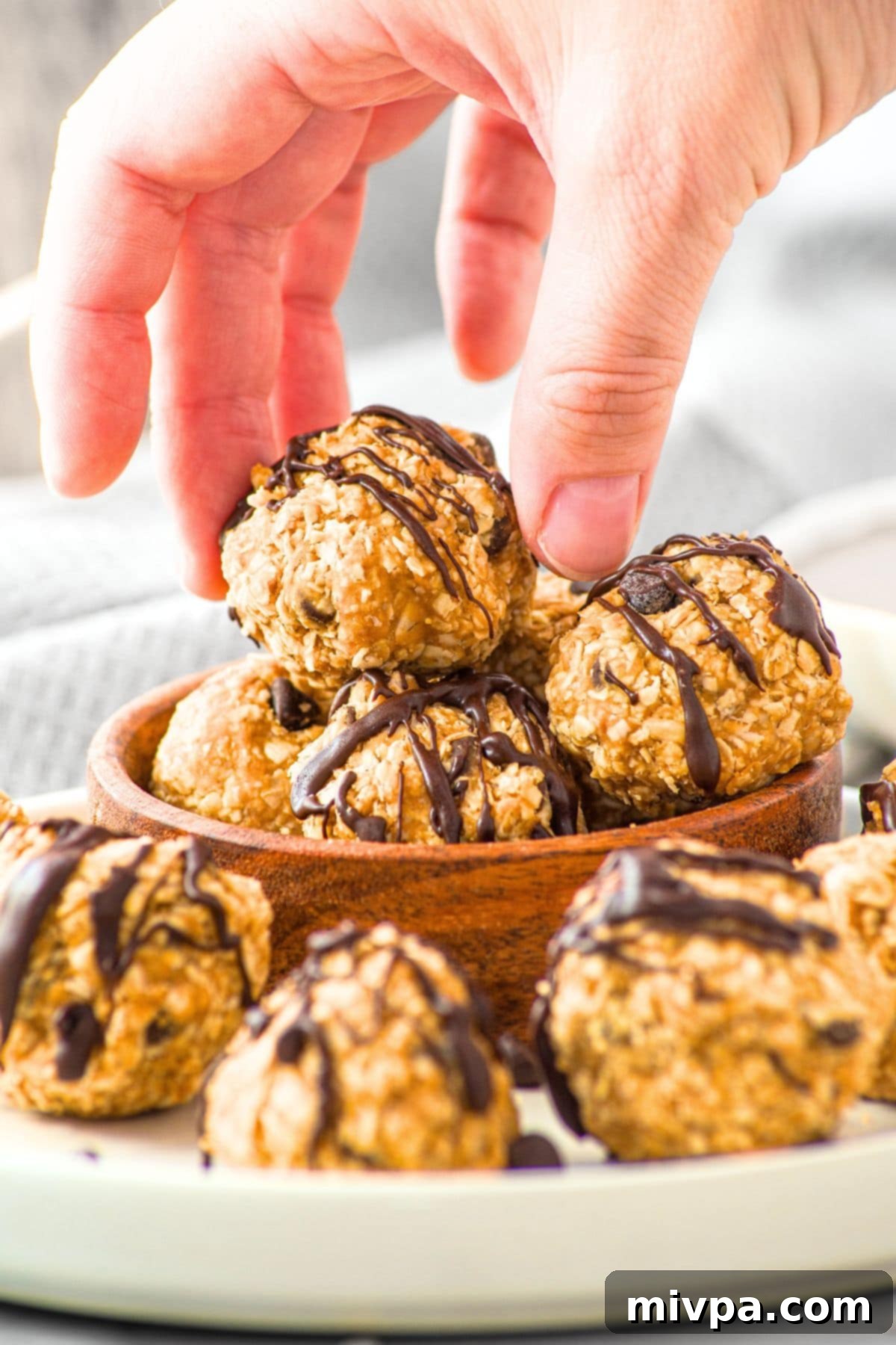 Oatmeal Peanut Butter Balls (Gluten-Free, Vegan) Hand reaching for an oatmeal peanut butter ball from bowl