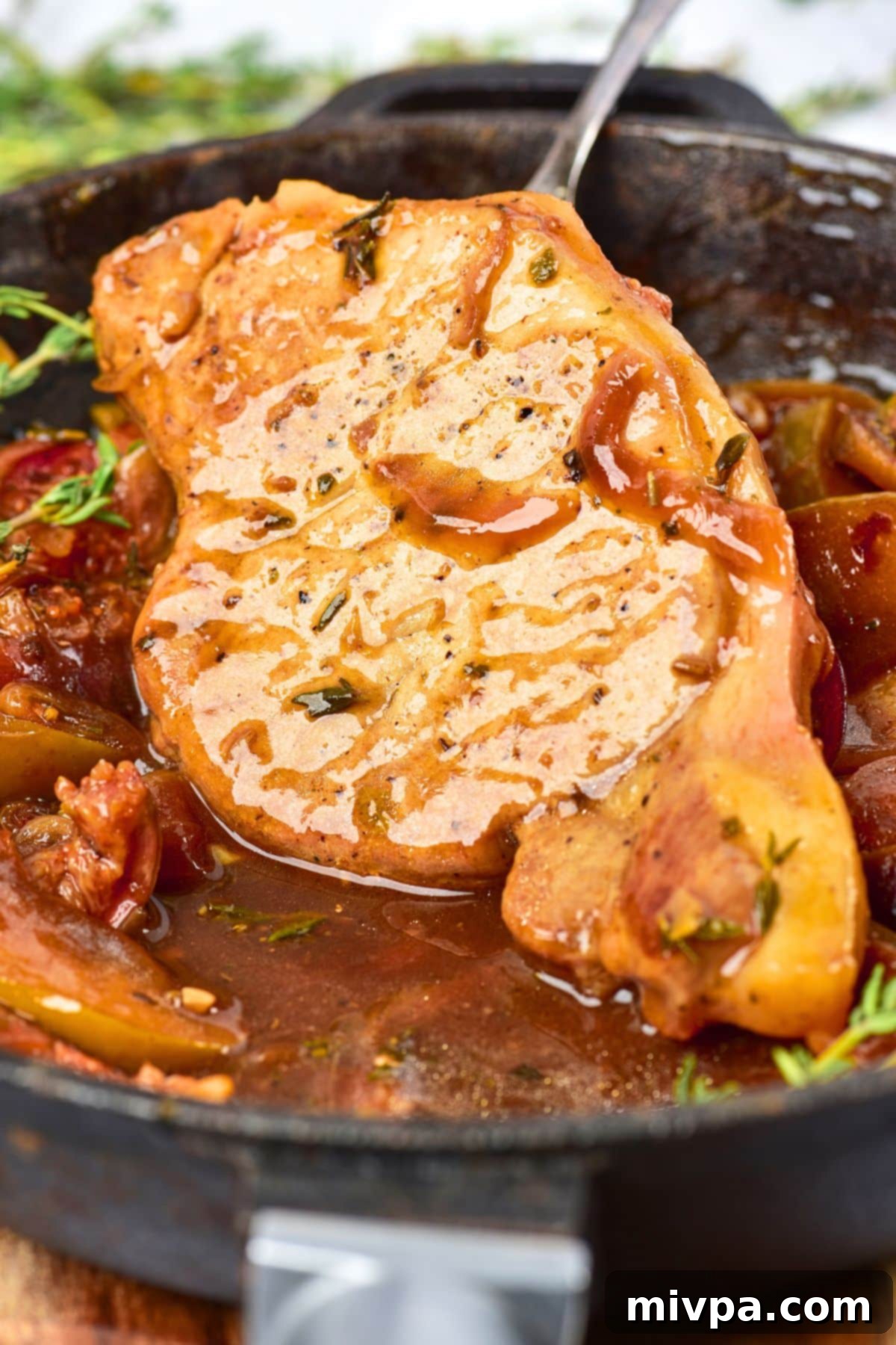 Gluten-Free Pork Chops and Apples Holding up a pork chop in a skillet of gravy with apples and figs