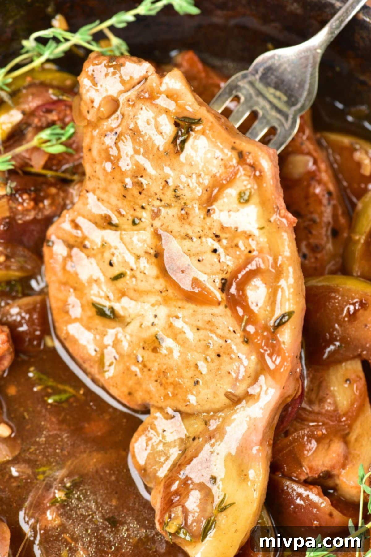 Pork Chops with Onions and Apples A fork lifting a piece of perfectly cooked pork chop from the skillet