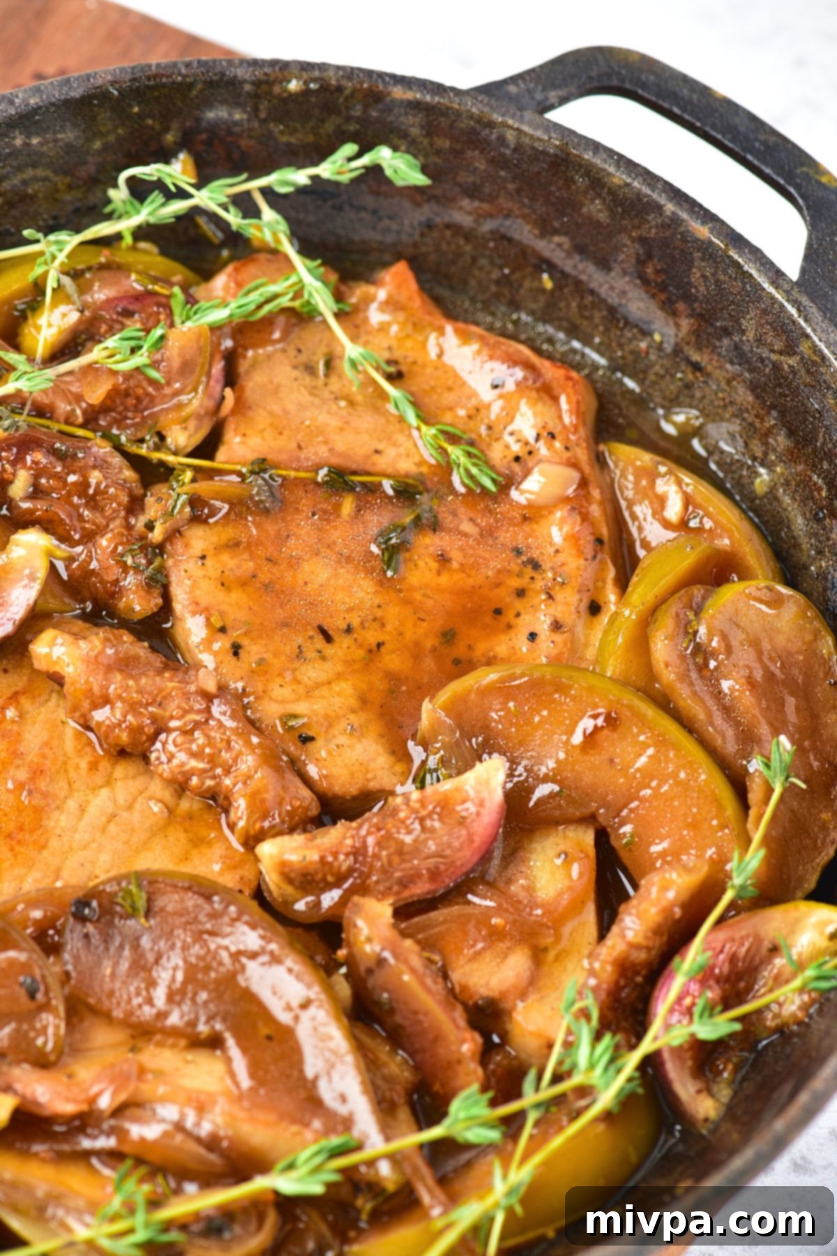 Pork Chops with Apples and Figs Up close view of golden brown caramelized apples and juicy pork chops in a cast iron skillet
