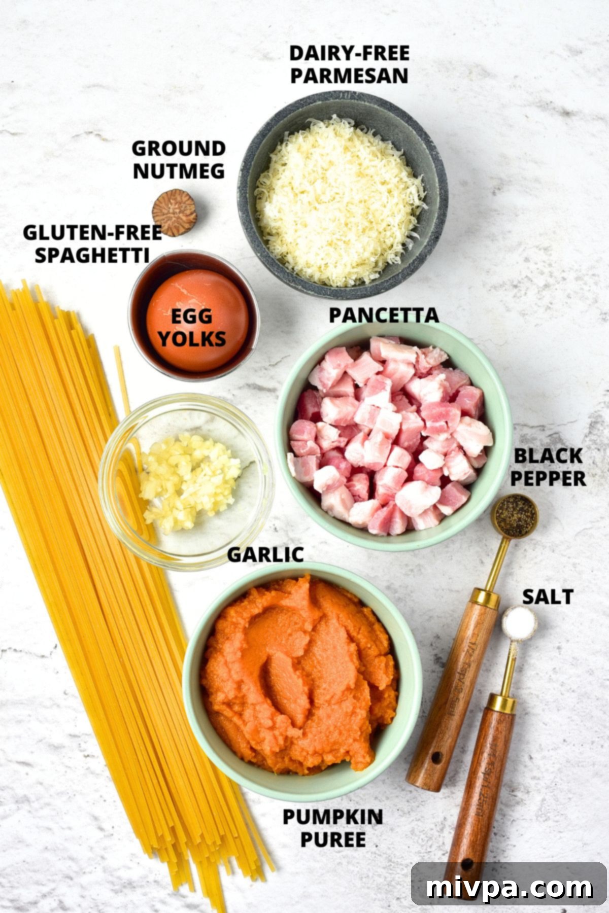 Pumpkin Carbonara Recipe (Gluten-Free, Dairy-Free Ingredients) Ingredients for pumpkin carbonara recipe laid out on a clean white board, including pasta, pumpkin puree, pancetta, and spices.
