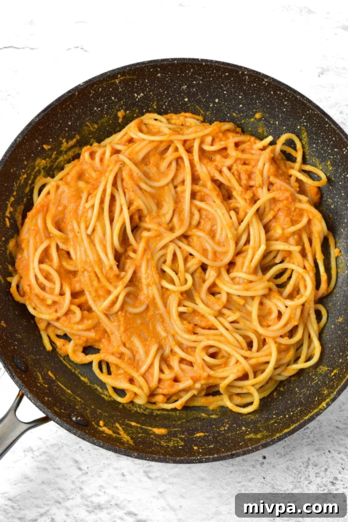 GF Carbonara Pasta Tossing Gluten-free pasta being tossed in orange pumpkin sauce in a skillet.