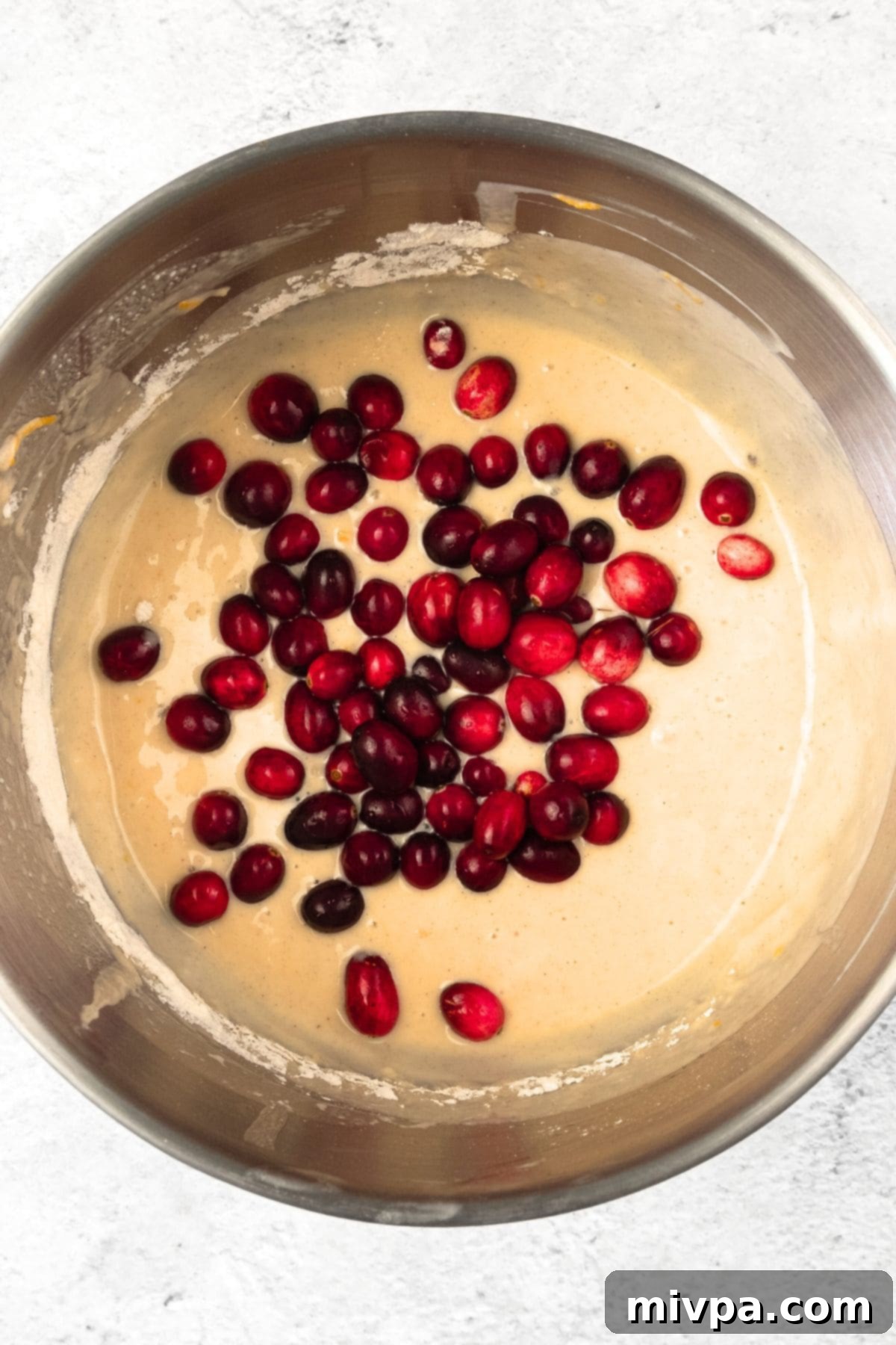How to Make Cranberry Orange Muffins Fresh cranberries being gently folded into the pale yellow muffin batter.