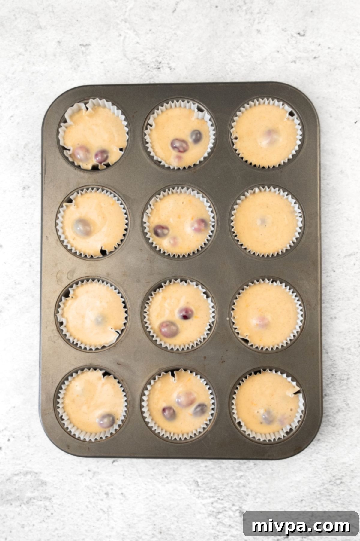 Gluten-Free Cranberry and Orange Muffins Cranberry muffin batter scooped into a lined muffin pan, ready for baking.