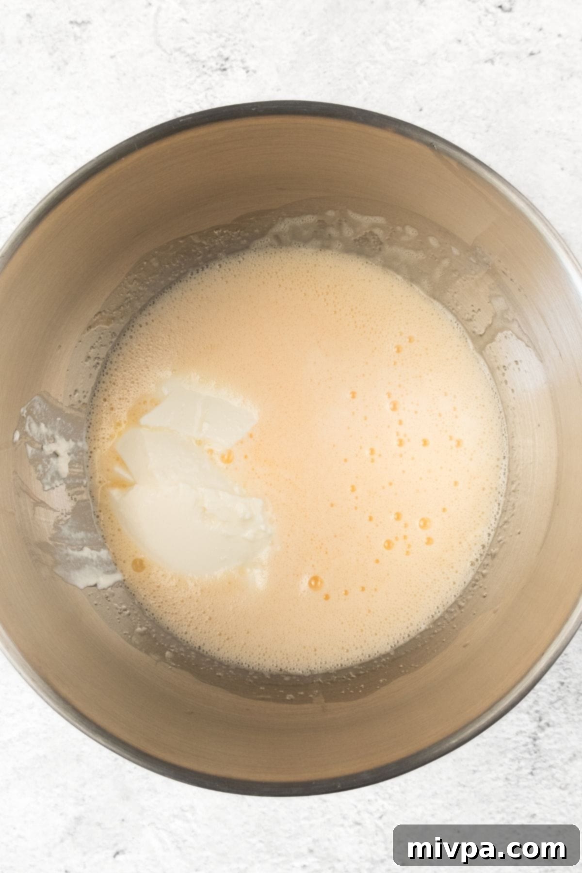 How to Make Cranberry and Orange Muffins Pale yellow muffin batter with yogurt added in a metal bowl.