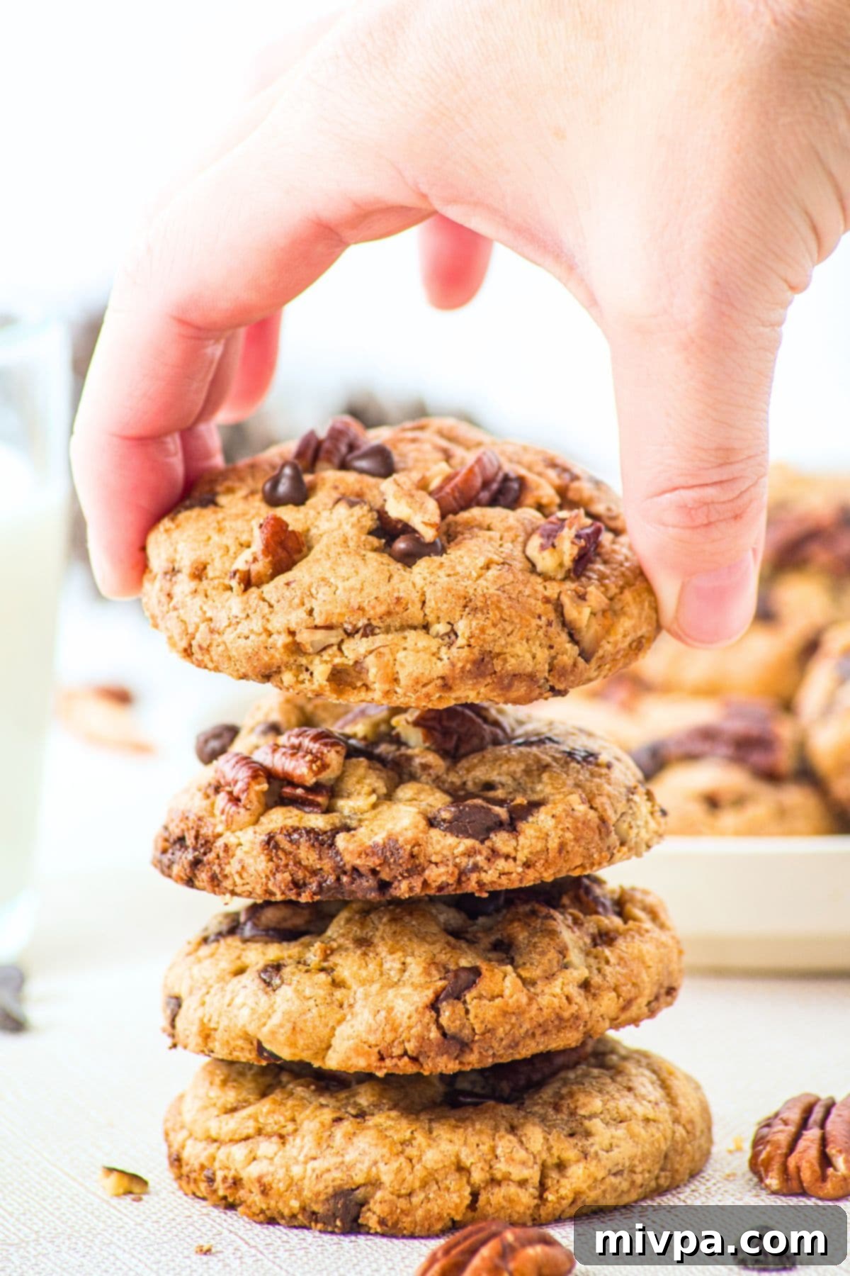Brown Butter Chocolate Chip Pecan Cookies (Gluten-Free) A hand reaching for a stack of freshly baked brown butter chocolate chip pecan cookies.