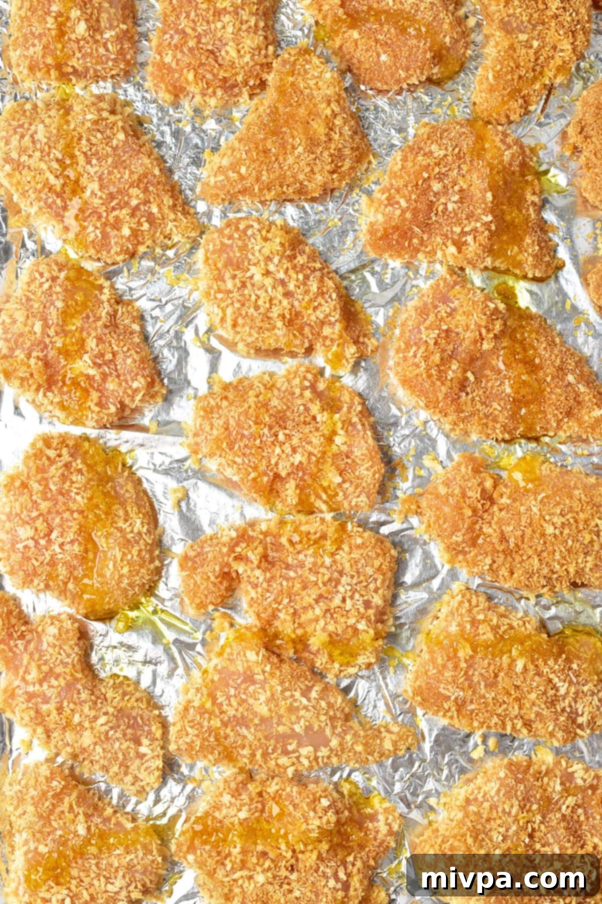 Homemade Turkey Nuggets (Gluten-Free, Dairy-Free) Bread crumb coated turkey pieces arranged on aluminum foil on a baking sheet.
