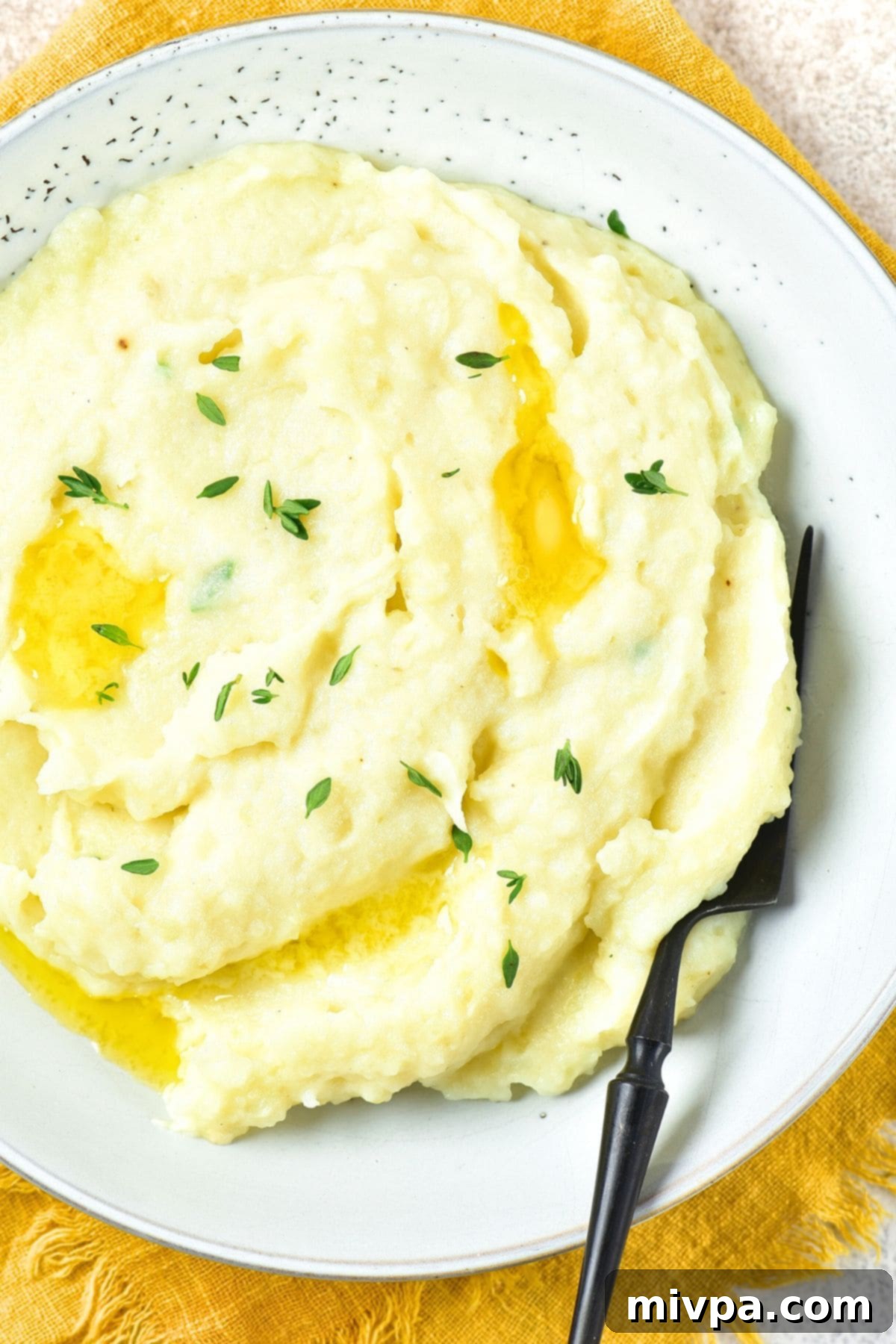 Creamy Roasted Garlic Mashed Potatoes (Gluten-Free, Vegan) Top down view of a bowl of creamy garlic mashed potatoes topped with fresh thyme.