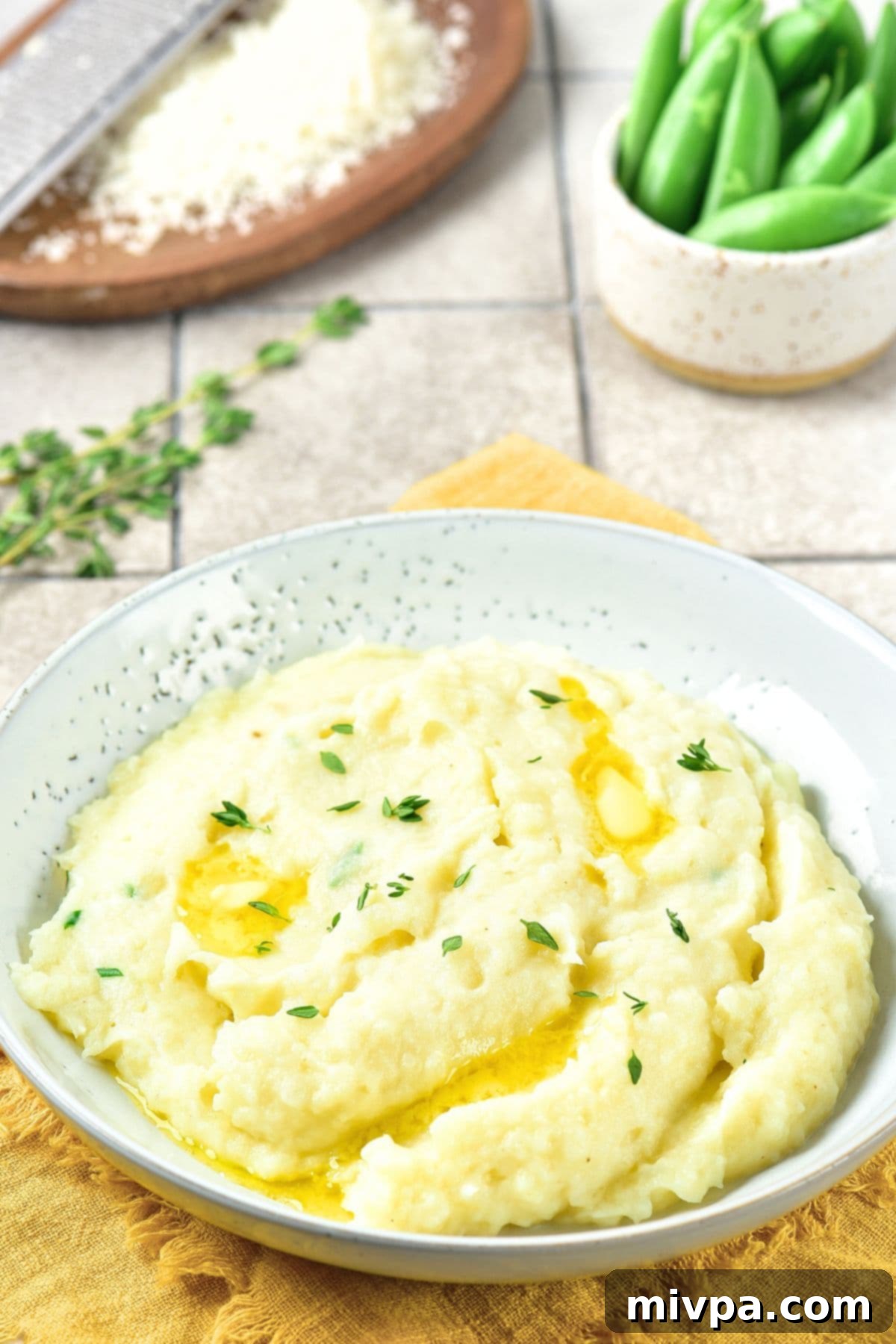 Roasted Garlic Mashed Potatoes (Gluten-Free, Vegan) A bowl of roasted garlic mashed potatoes on a board sprinkled with fresh thyme.