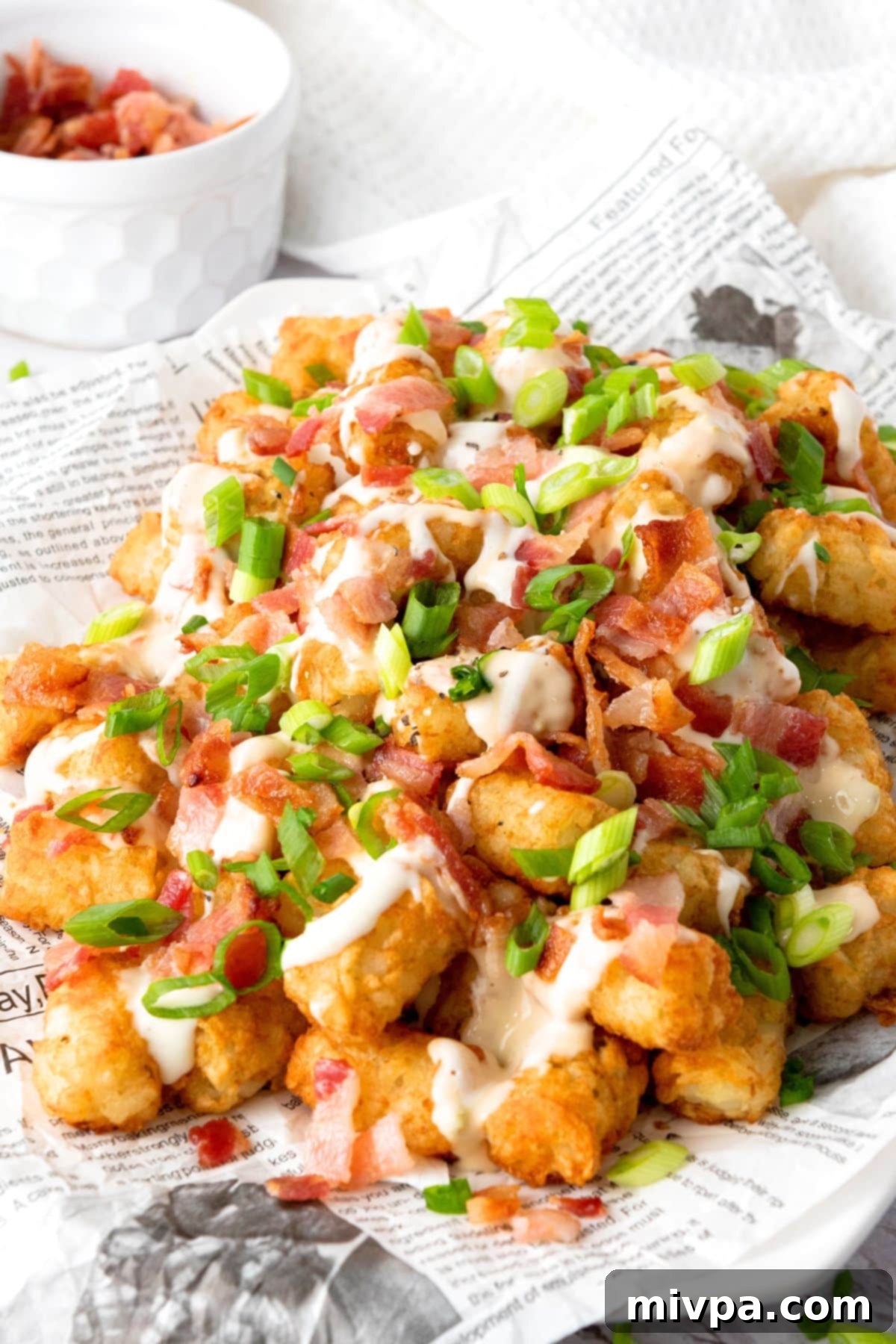 Loaded Tater Tots (Gluten-Free) Loaded tater tots on parchment paper with bowl of bacon.